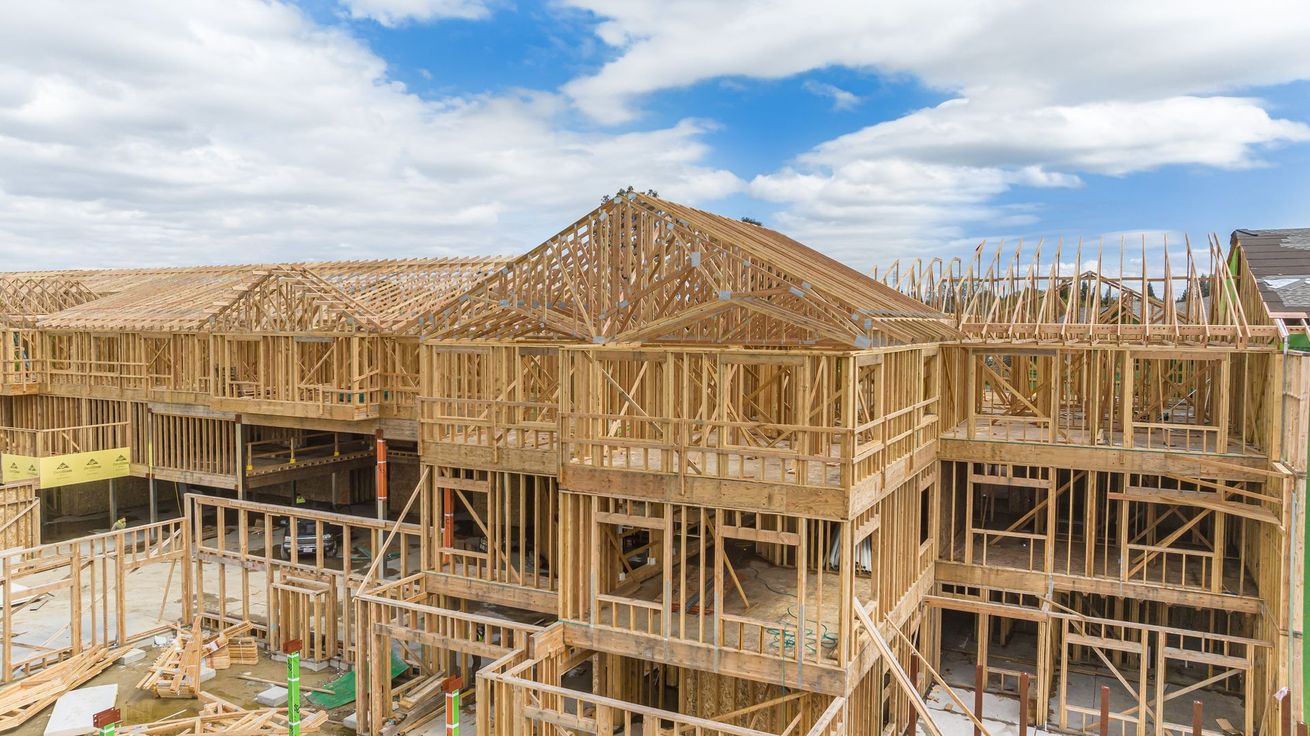 New homes under construction with wooden framing against a partly cloudy blue sky