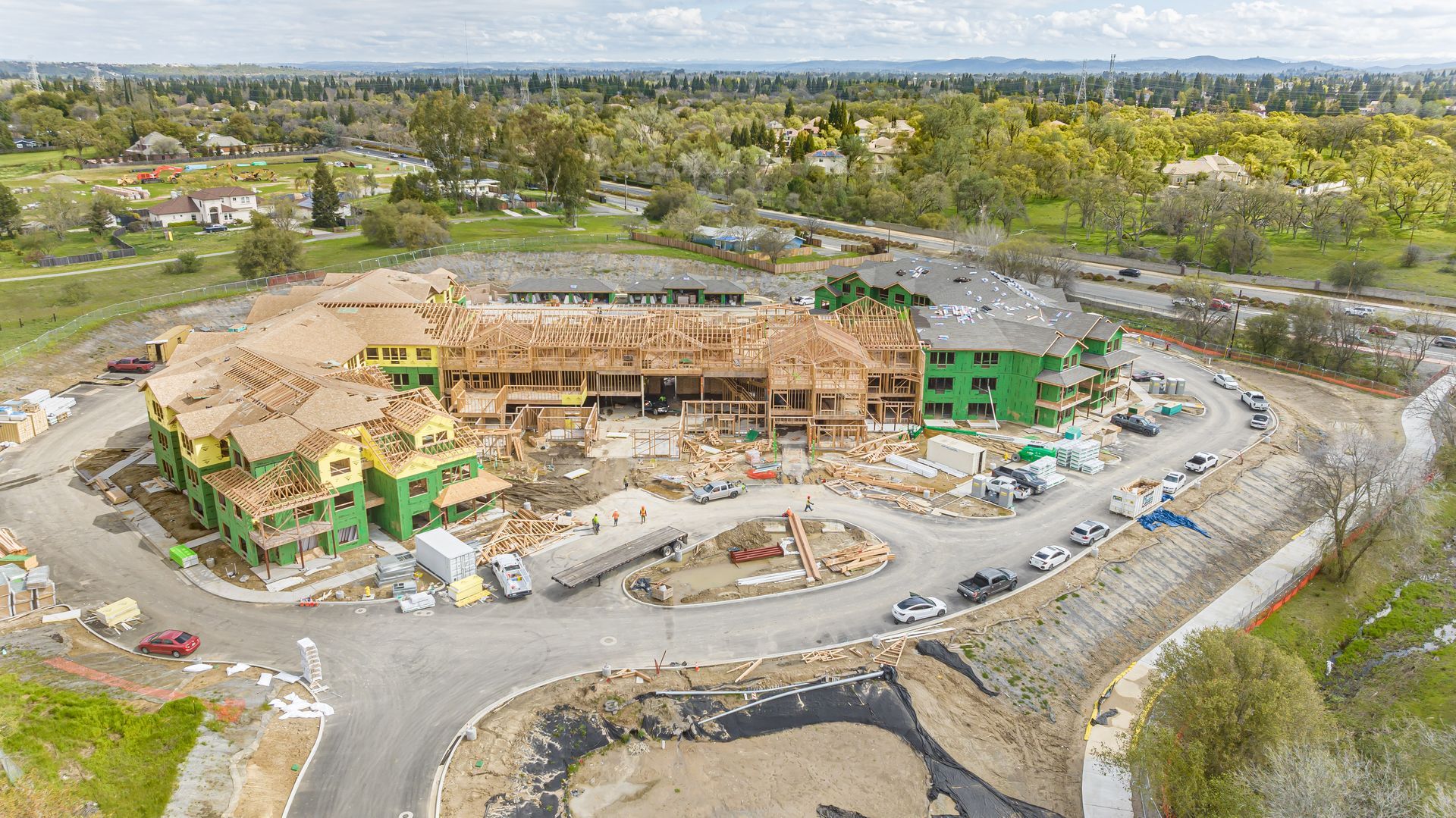 Aerial view of a large building under construction with scaffolding, machinery, and a curving access road.