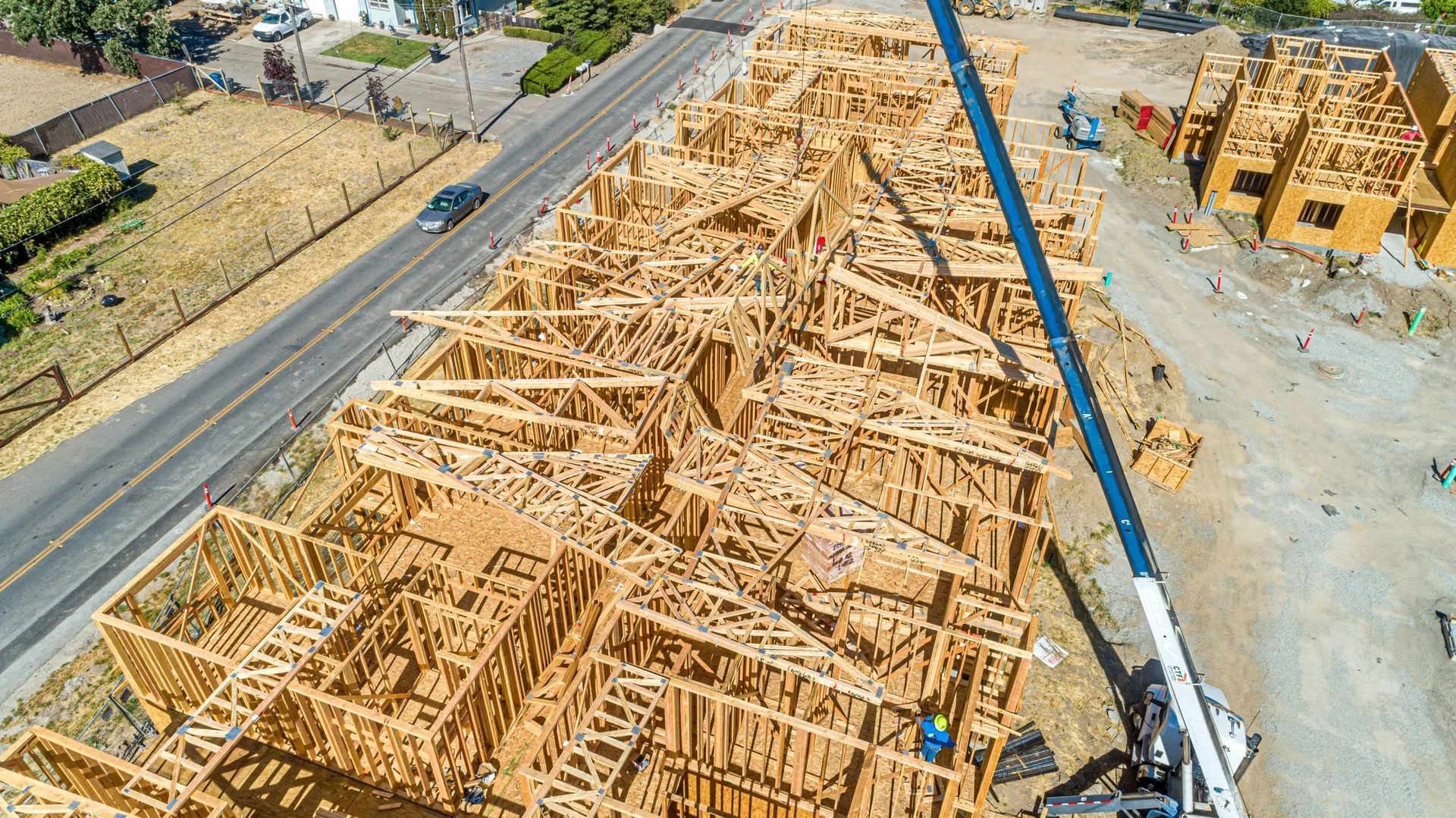 An aerial view of a wooden building construction site with a crane arm extending over the roof trusses.