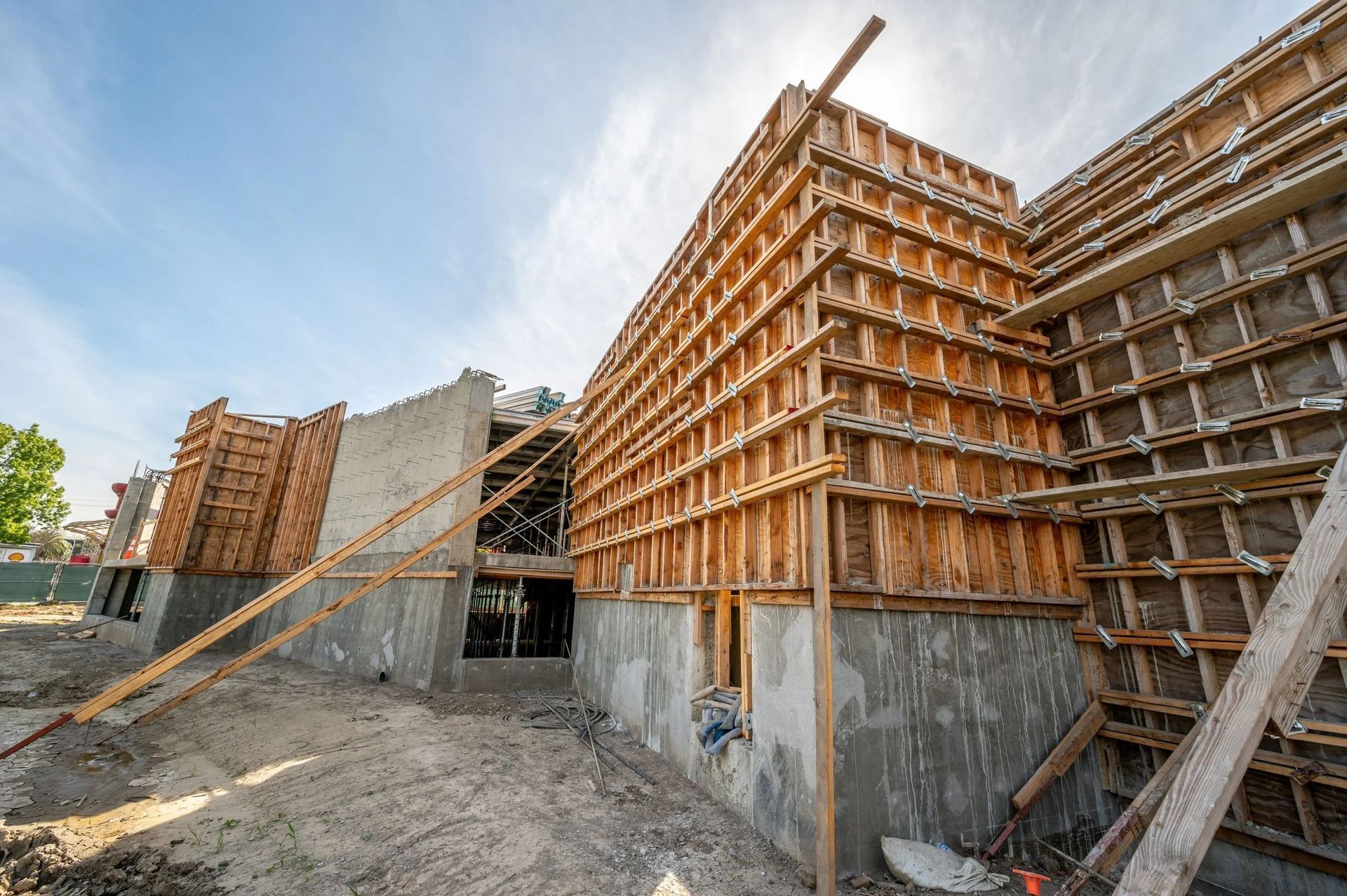 A construction site showing tall wooden formwork for a concrete wall against a bright, sunny sky.