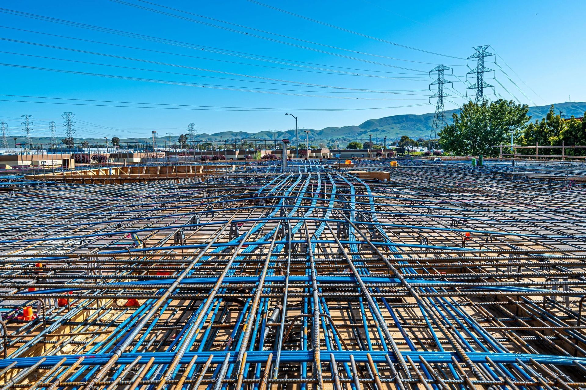 A vast construction site featuring an extensive network of blue electrical conduits laid out on a steel rebar grid.