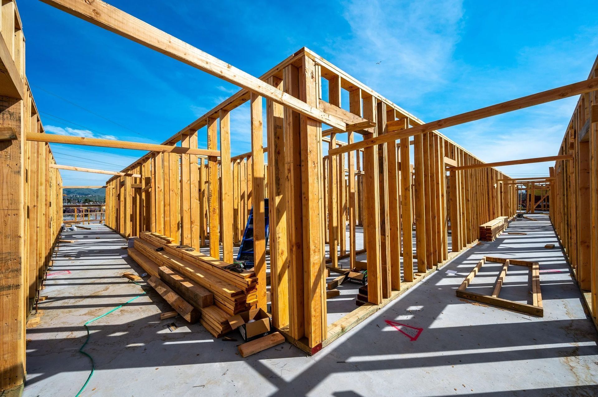 Wooden framing for a building under construction on a concrete slab under a bright blue sky.