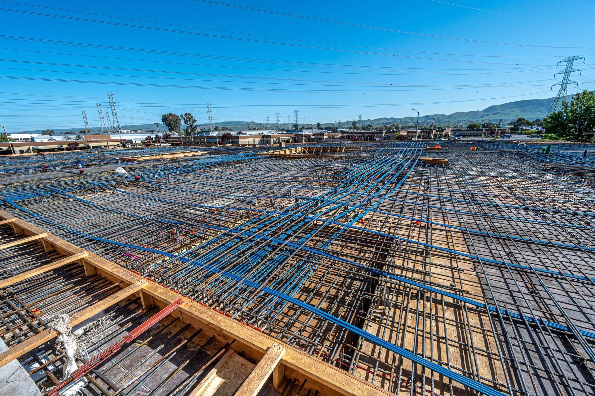 A construction site view of a large concrete slab foundation reinforced with a dense grid of steel rebar.