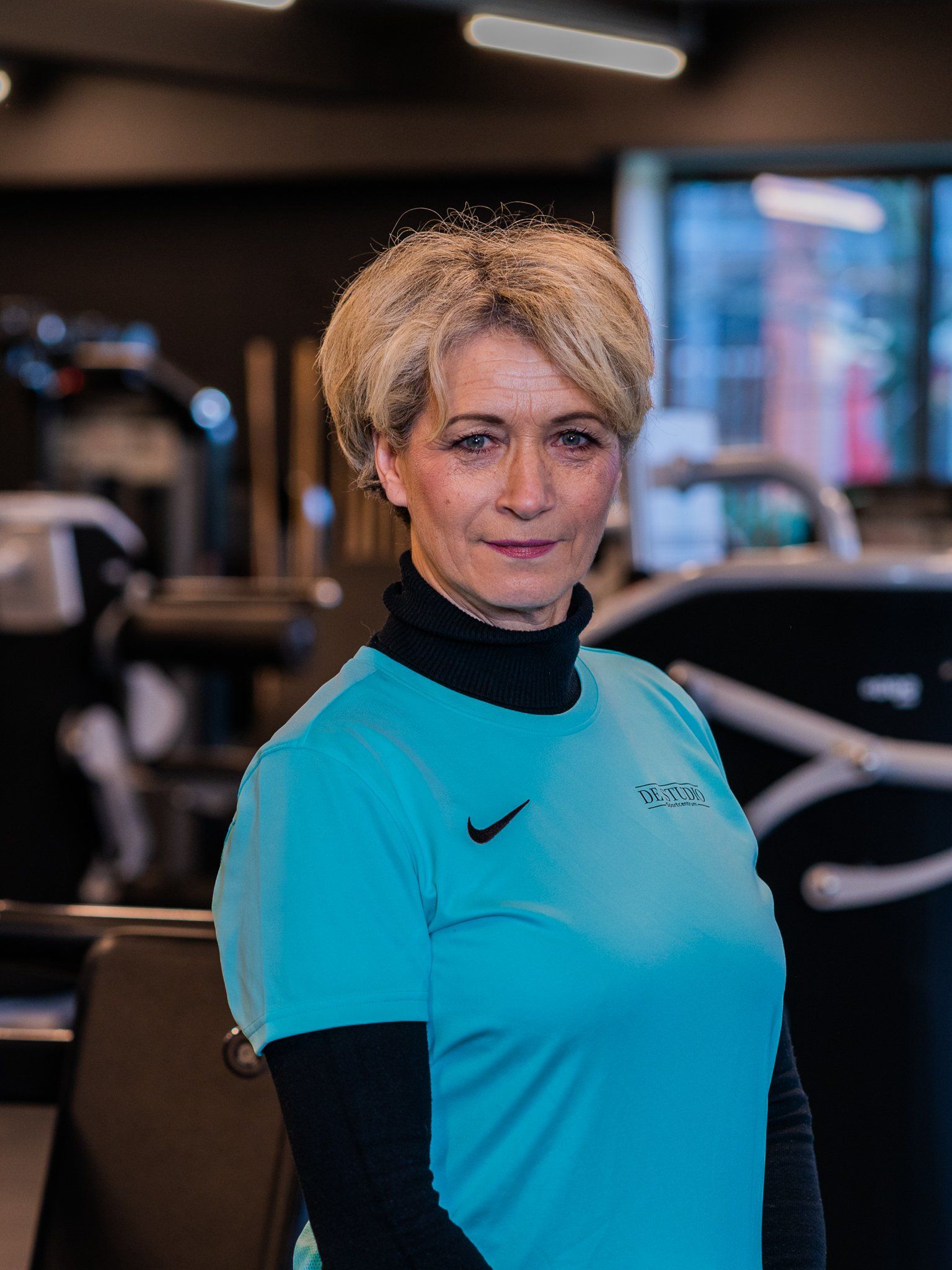 Een vrouw in een blauw shirt staat in een sportschool.