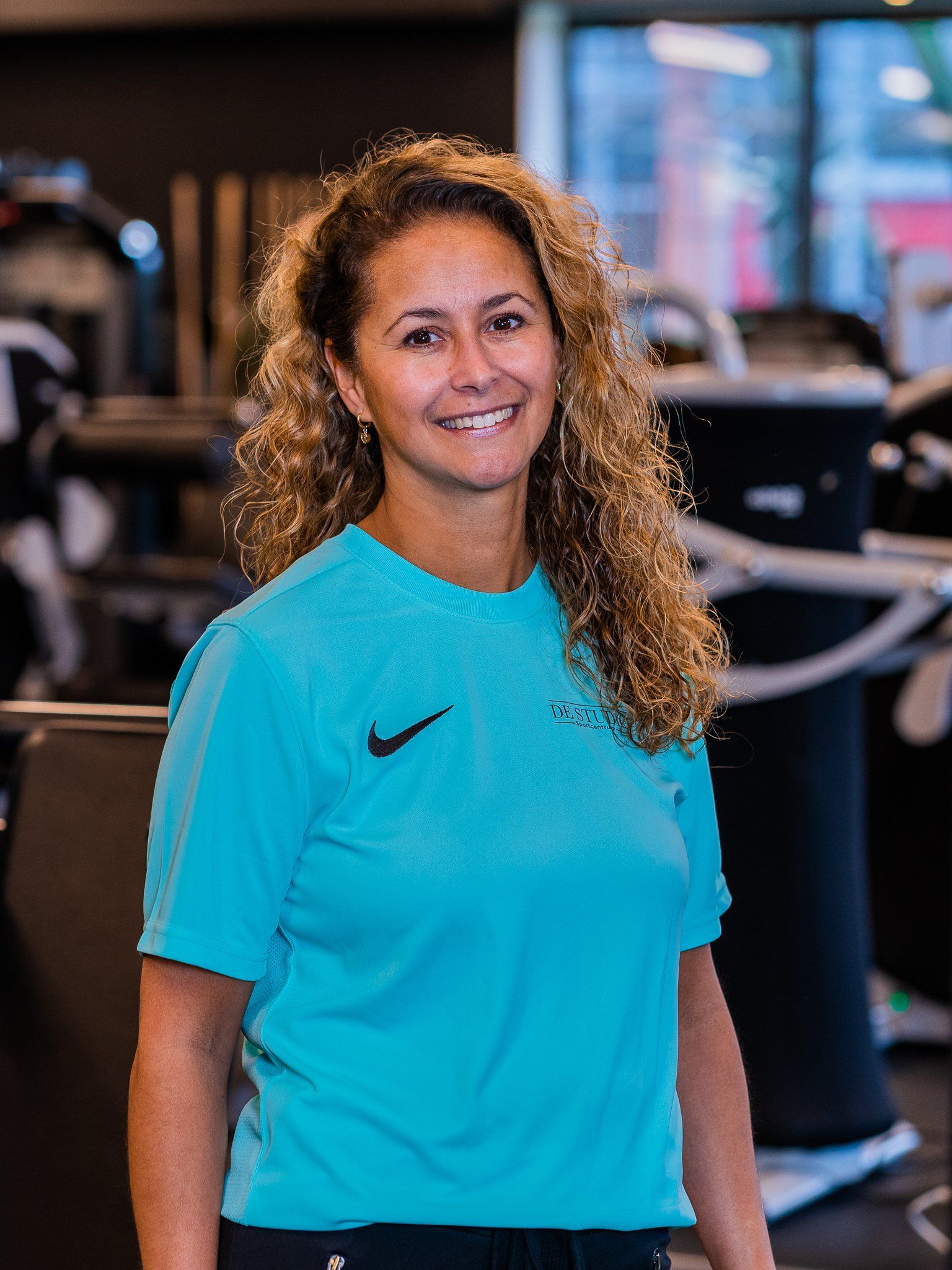 Een vrouw in een blauw Nike-shirt lacht in een sportschool.