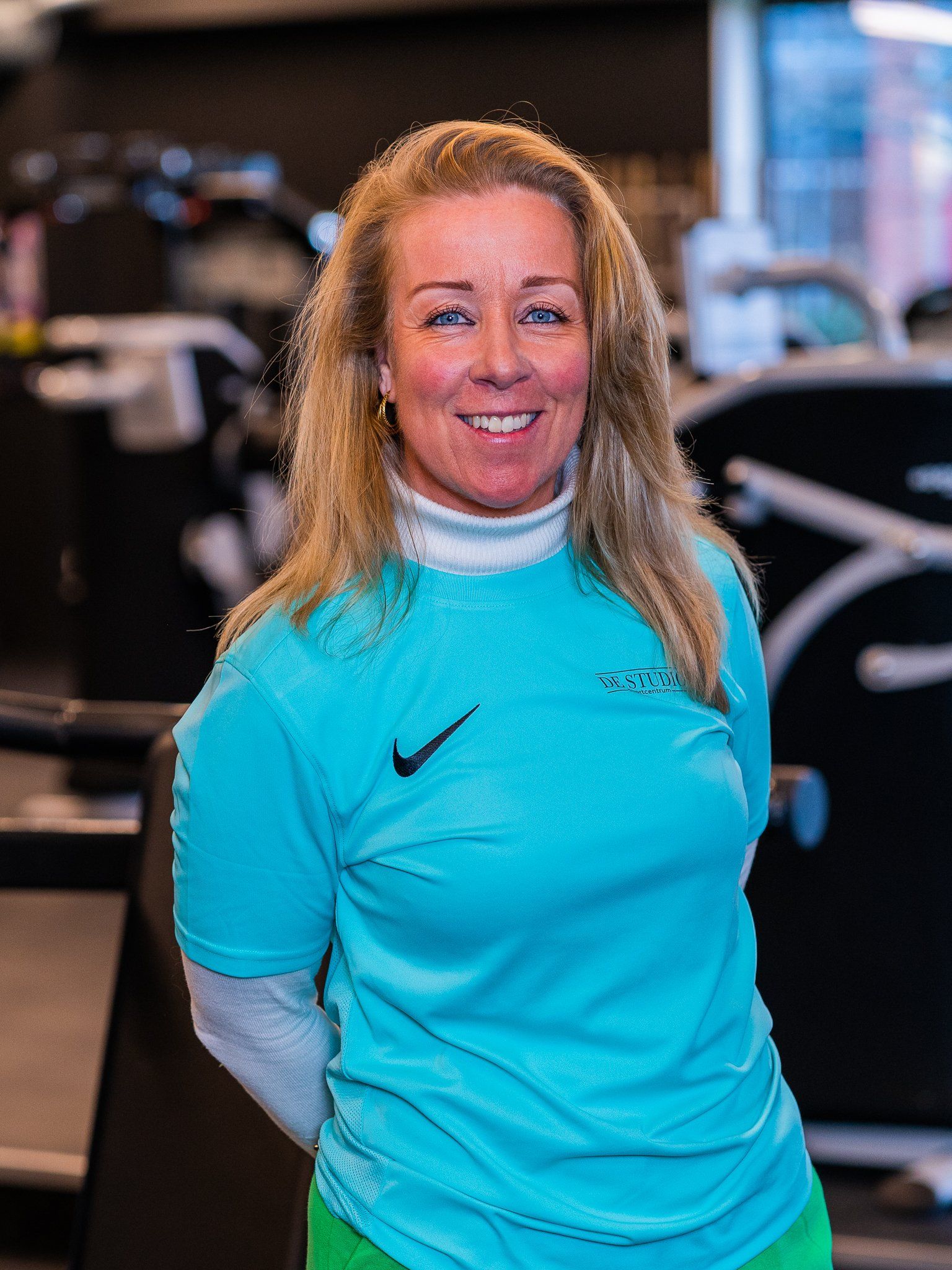 Een vrouw in een blauw Nike-shirt lacht in een sportschool.