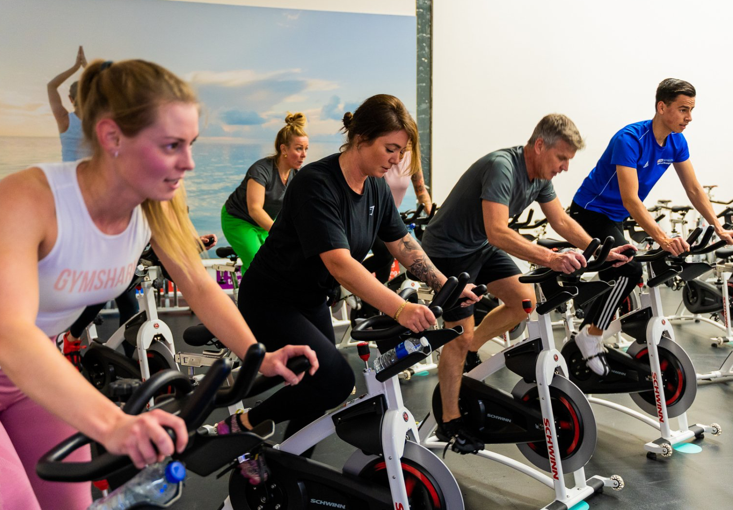 Een groep mensen fietst op hometrainers in een sportschool.
