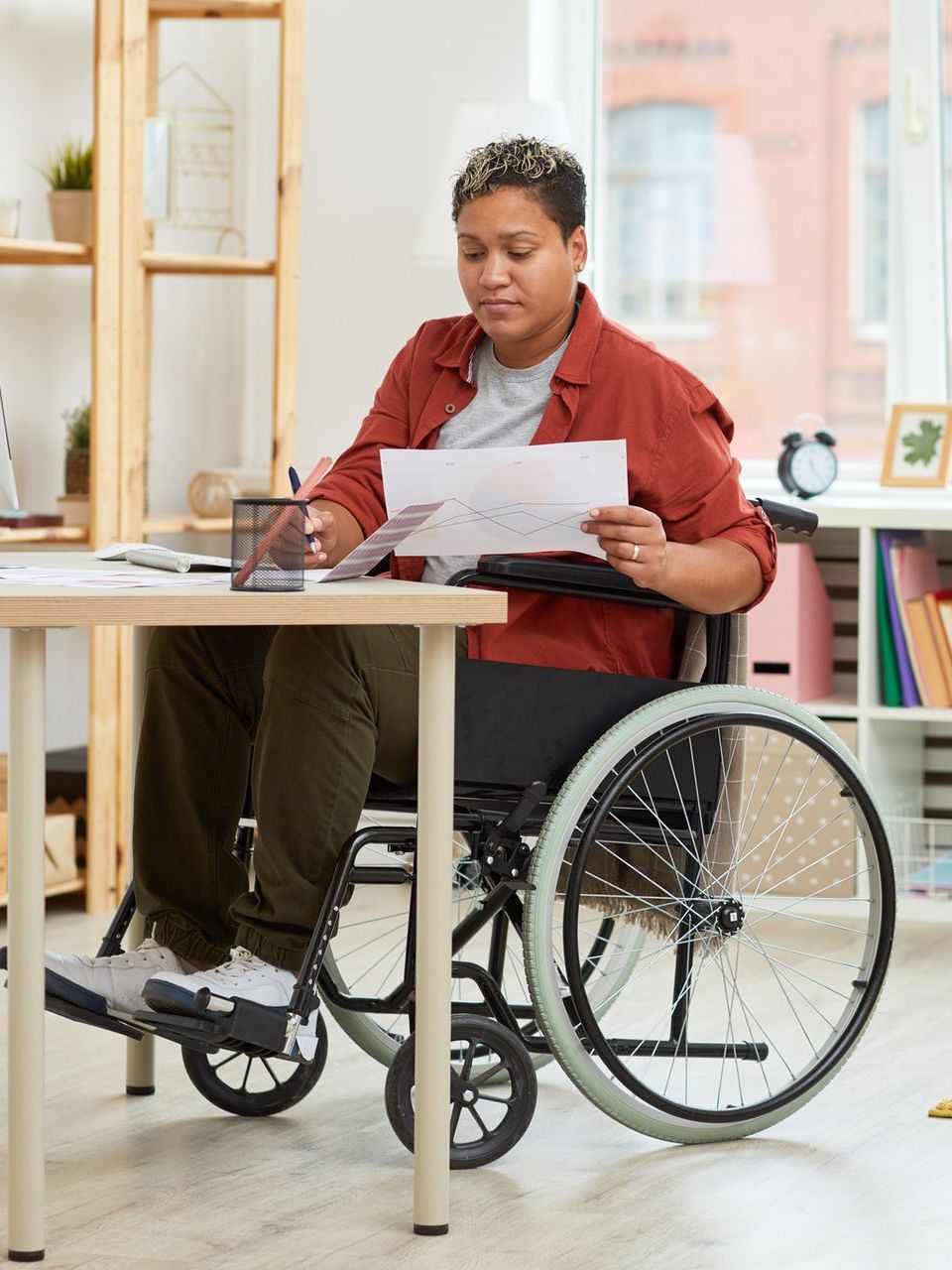 A woman in a wheelchair is sitting at a table reading a piece of paper.