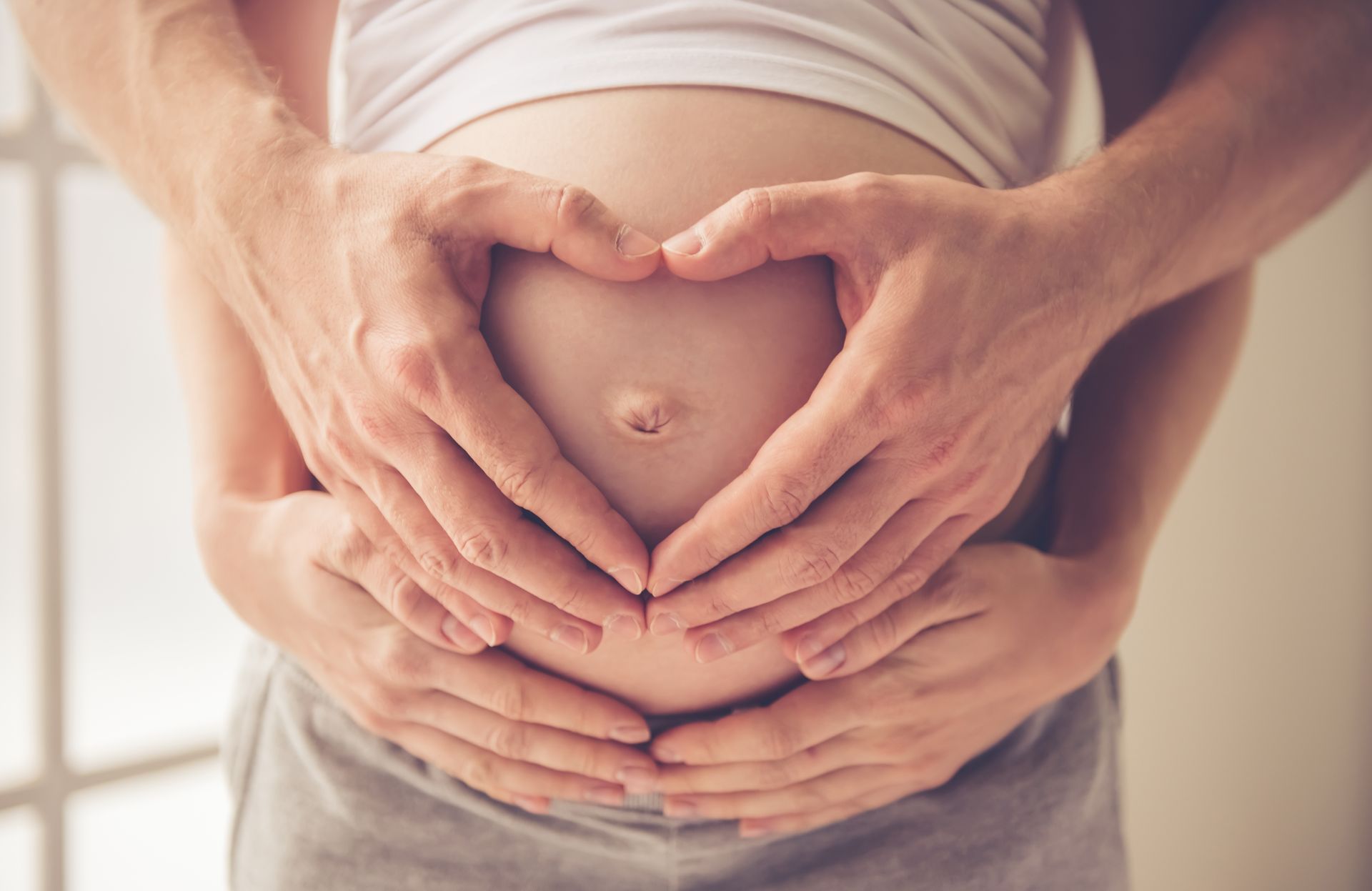 Hendur mynda hjarta yfir óléttri maga í hlýju ljósi
