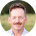 Smiling man with mustache in front of a blurred green background.