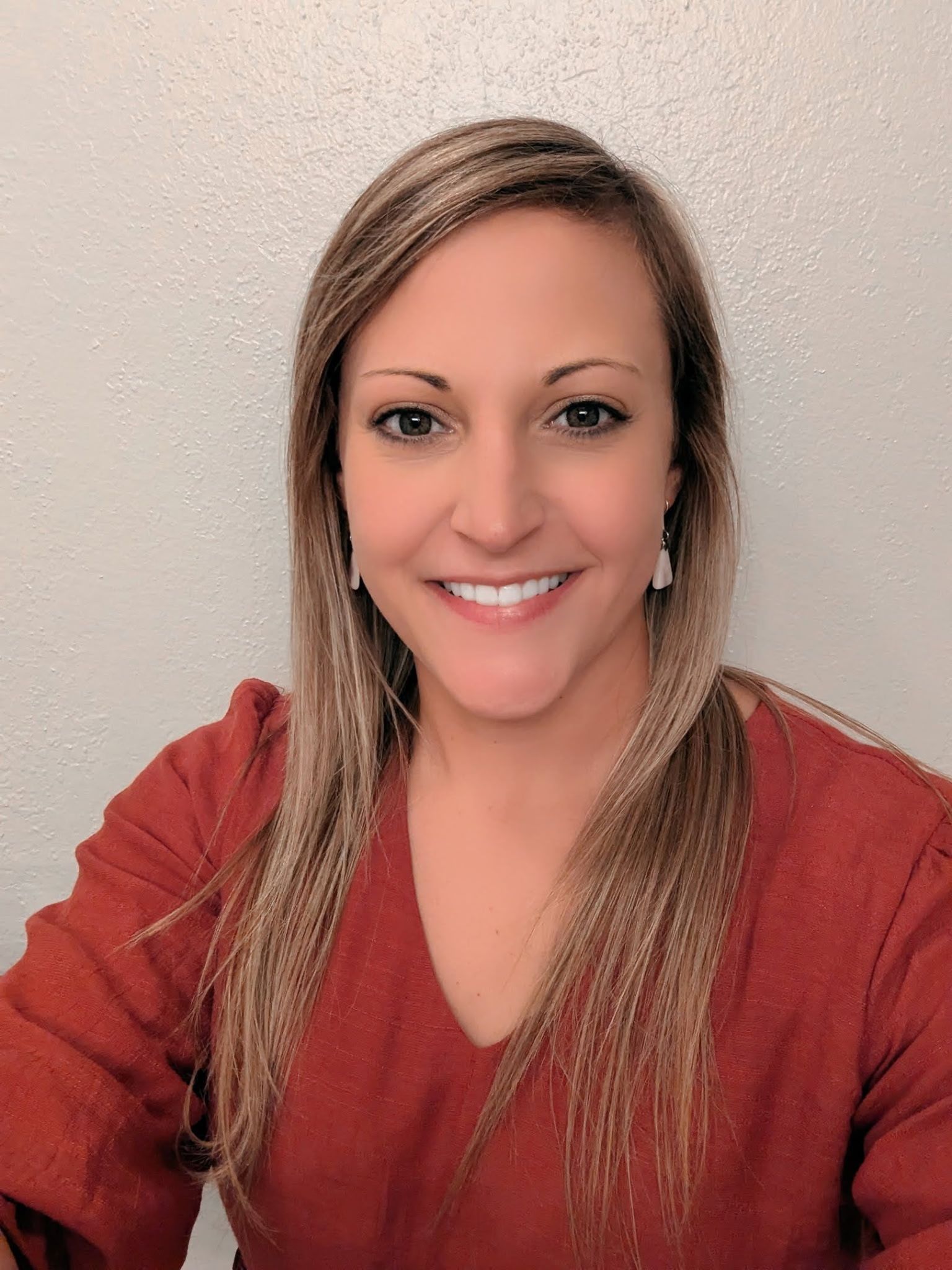 Smiling person in a red sweater against a light wall, facing the camera.