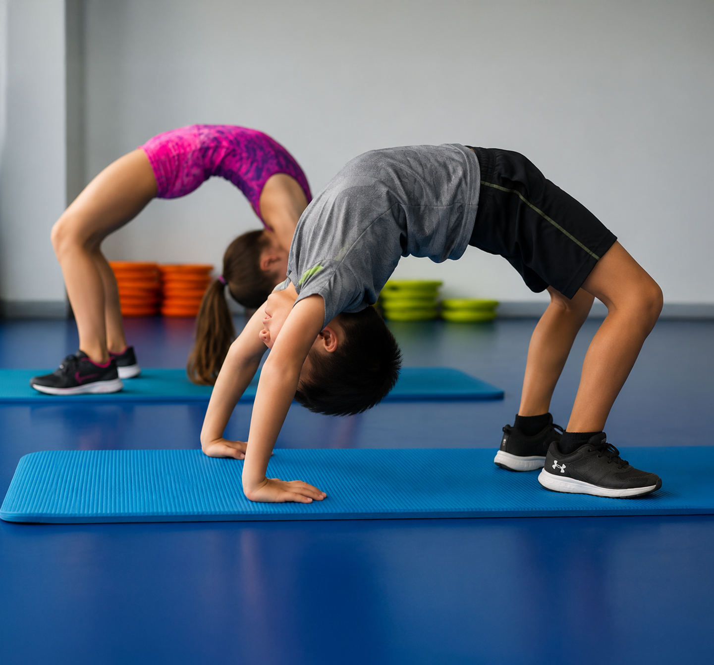 Two people doing backbends on yoga mats in a studio, with colorful stacked blocks in the background