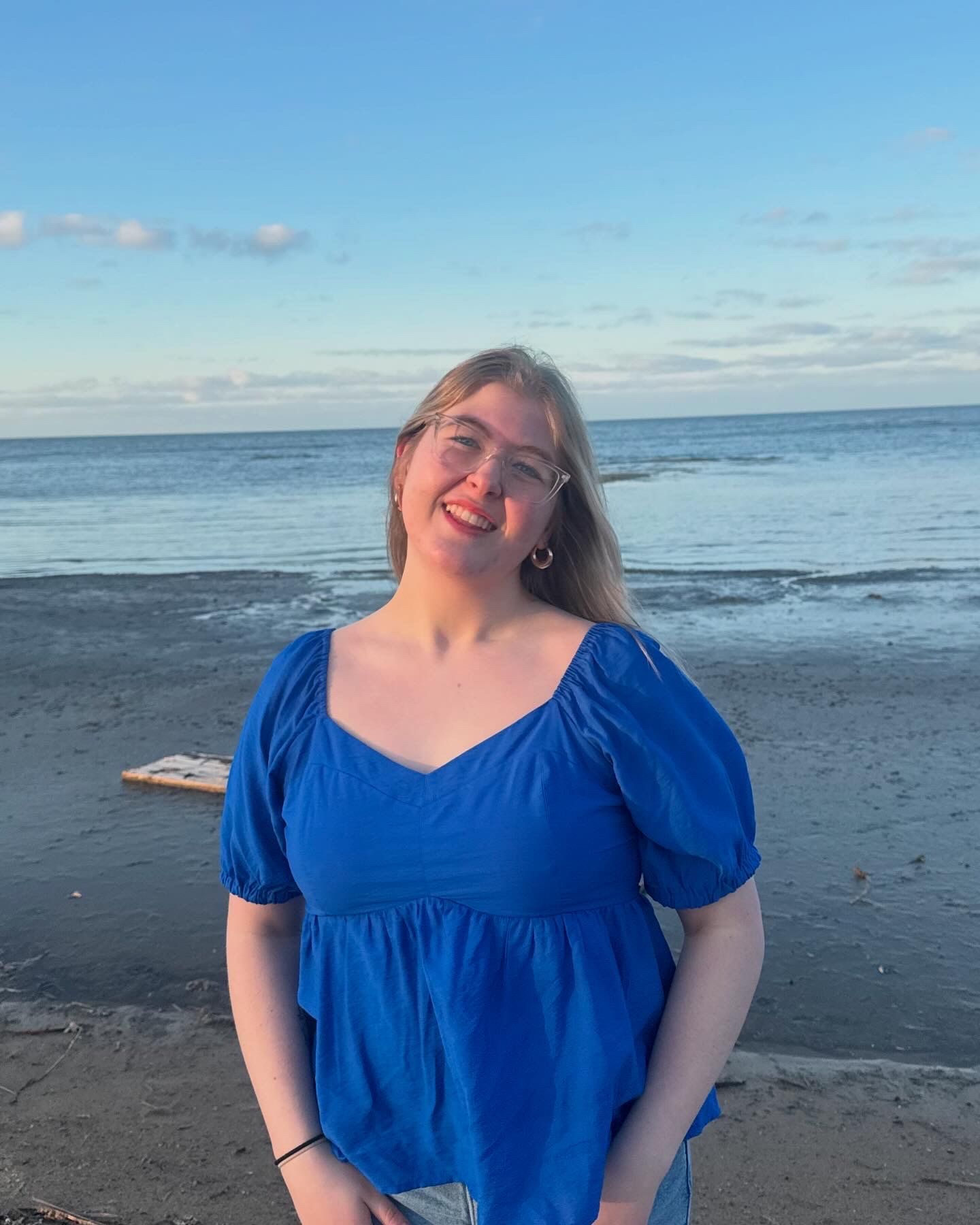 Person in a bright blue dress smiling on a beach with ocean and sky in the background