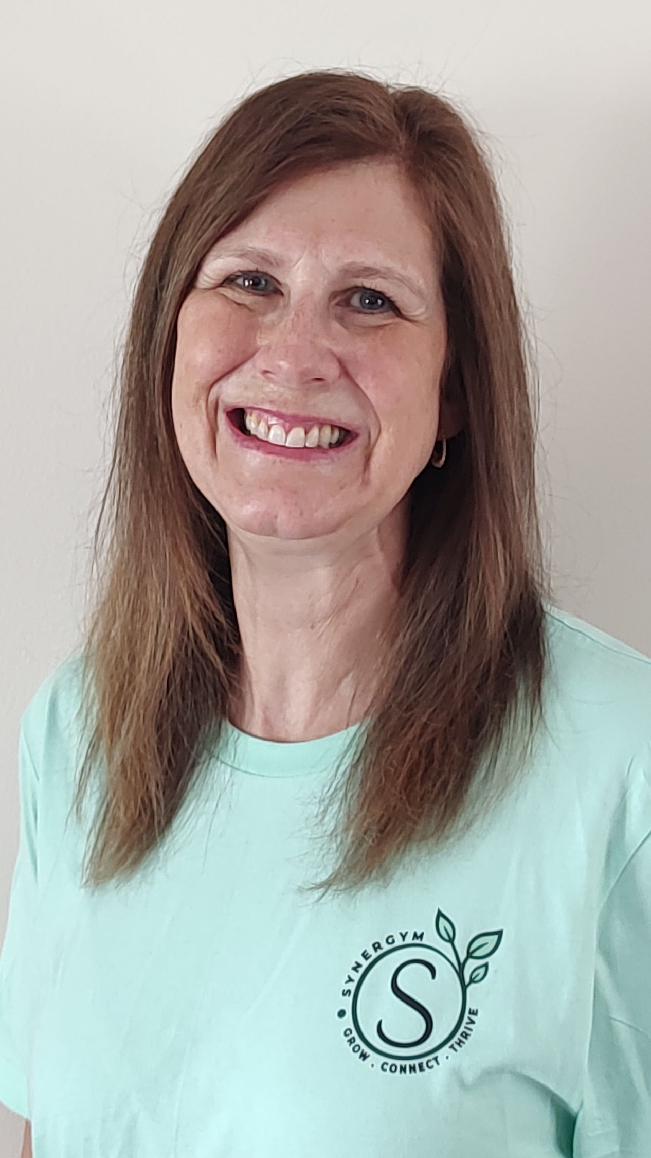 Smiling woman with long brown hair wearing a mint green shirt against a plain light background