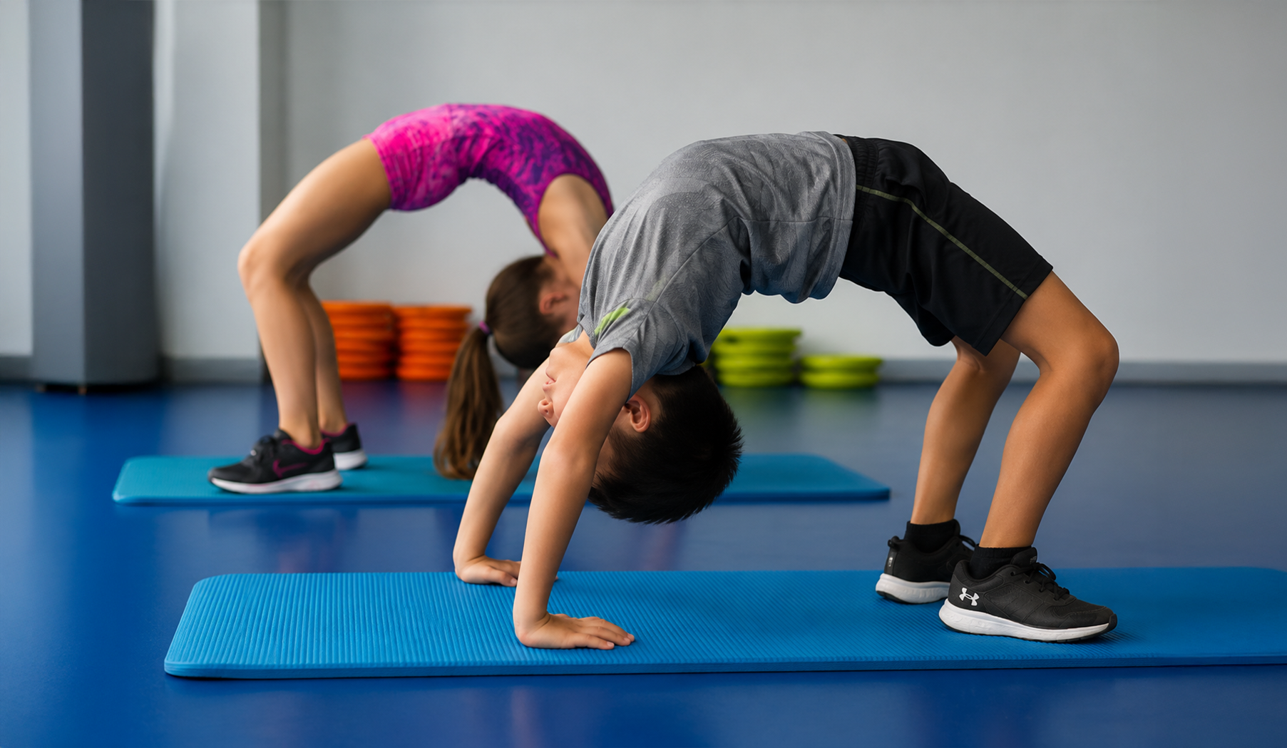 Two gymnasts practicing backbends on blue mats in a gym studio