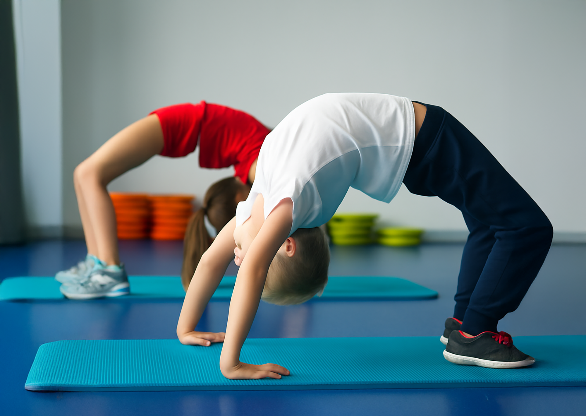 Two people doing backbends on yoga mats in a studio, one in red and one in white and navy.