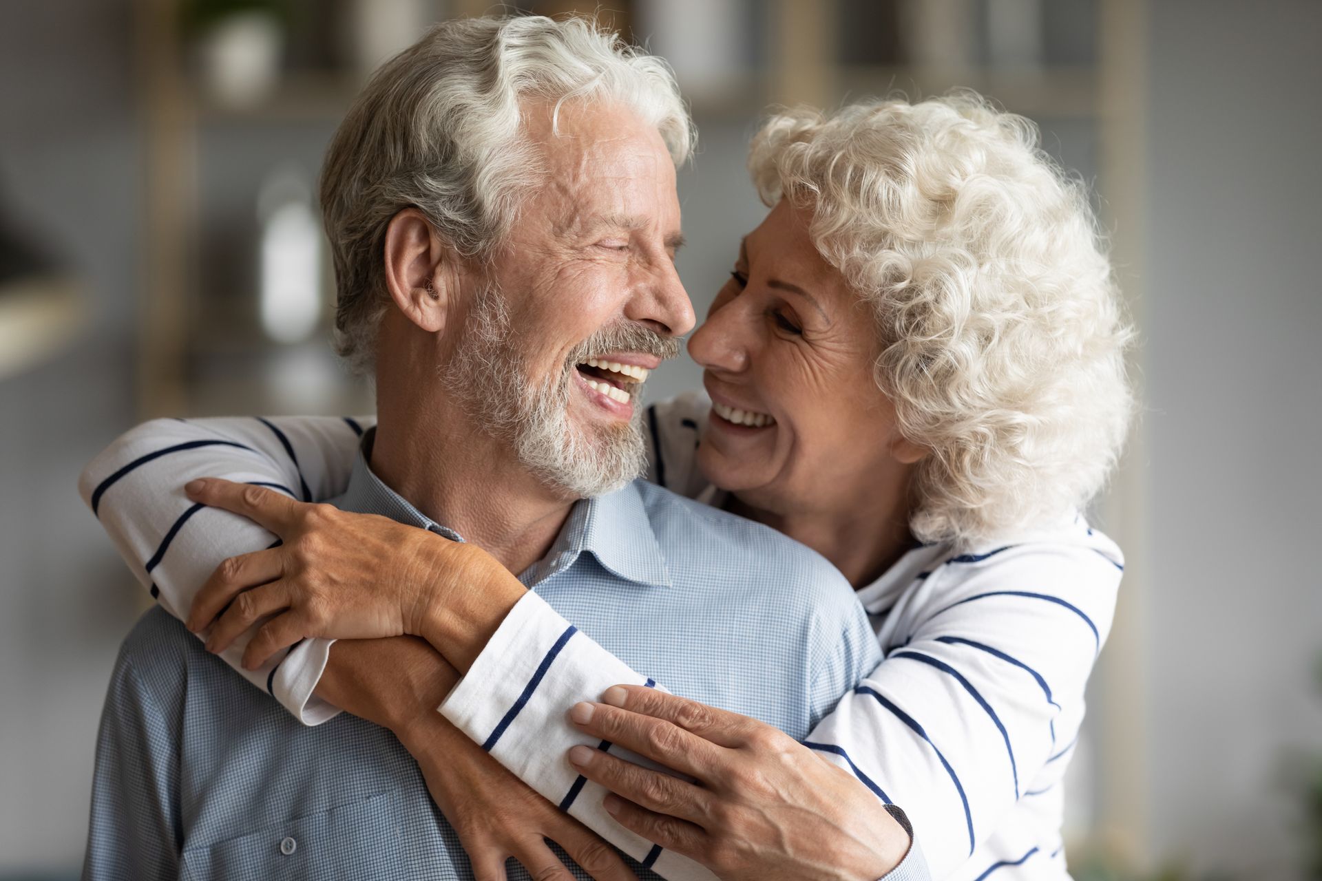 Two smiling seniors leaning close together outdoors in soft sunlight with green foliage behind them
