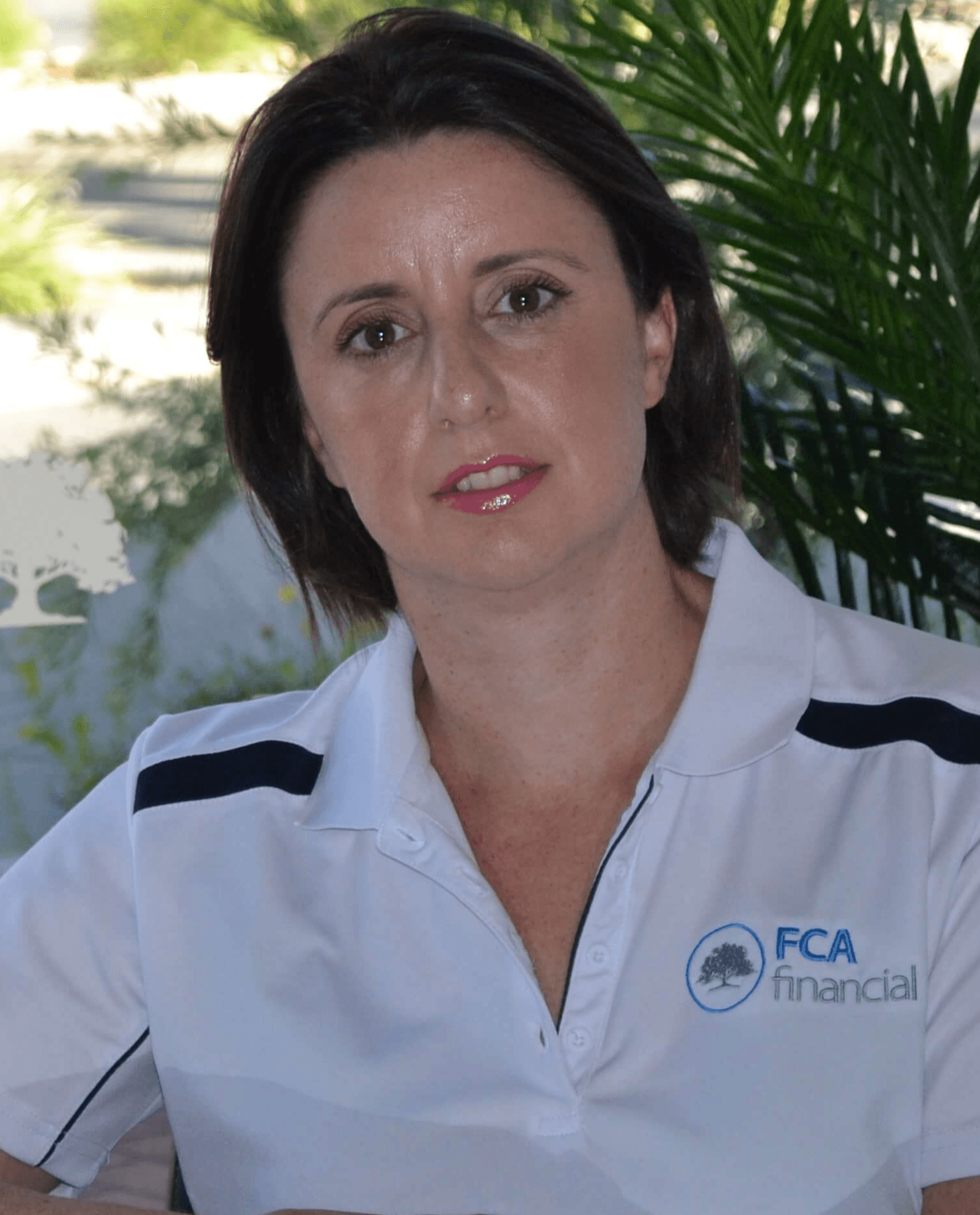 Woman in a white FCA Financial shirt standing outdoors with palm leaves in the background