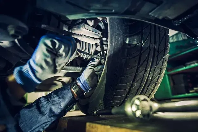 A man is working on the underside of a car in a garage.