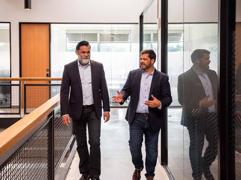 Two men in suits walking and talking in a modern office hallway