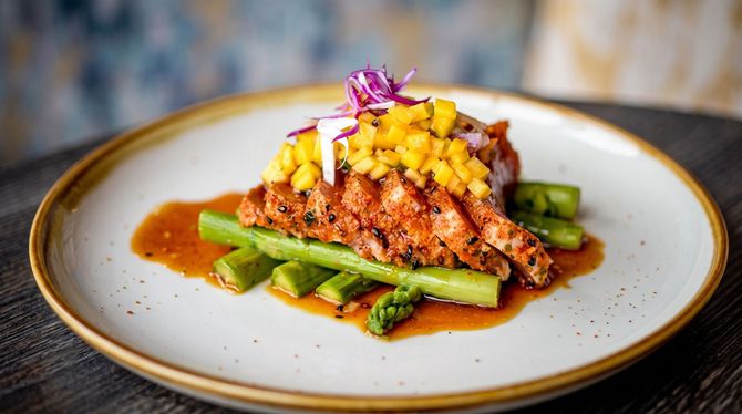 Plated seared fish with mango salsa and asparagus on a white dish with brown sauce