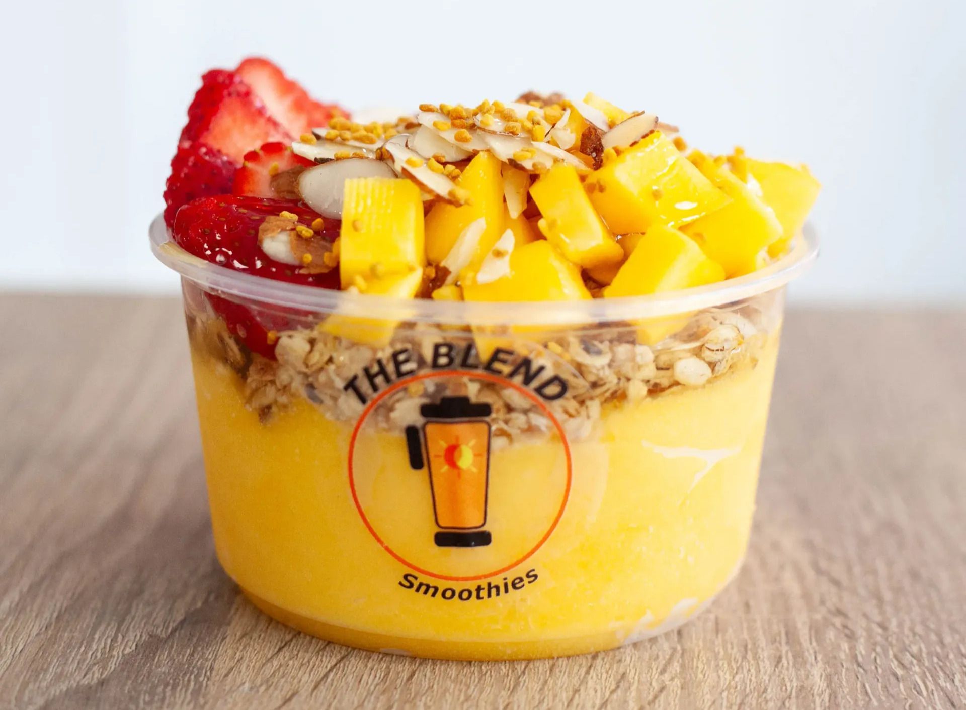 Acai bowl from The Blend, with mango, strawberries, granola, and almonds in a clear plastic cup.