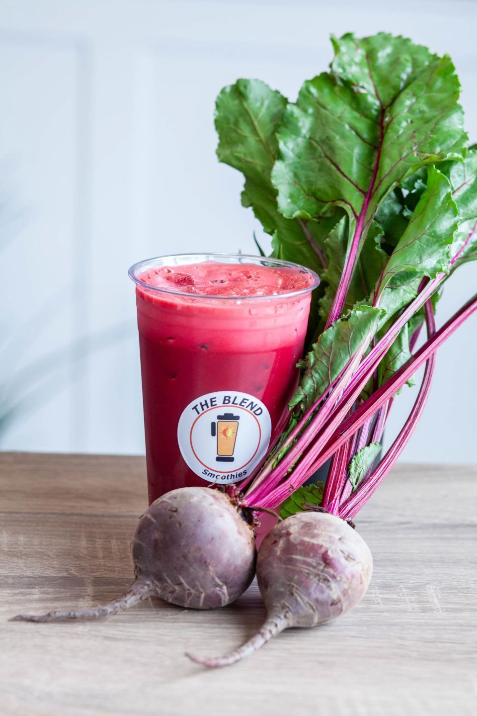 Beet juice in a plastic cup next to fresh beets with their stems and leaves on a wooden surface.