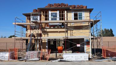 Two-story house under construction with scaffolding, unfinished siding, and construction materials in front