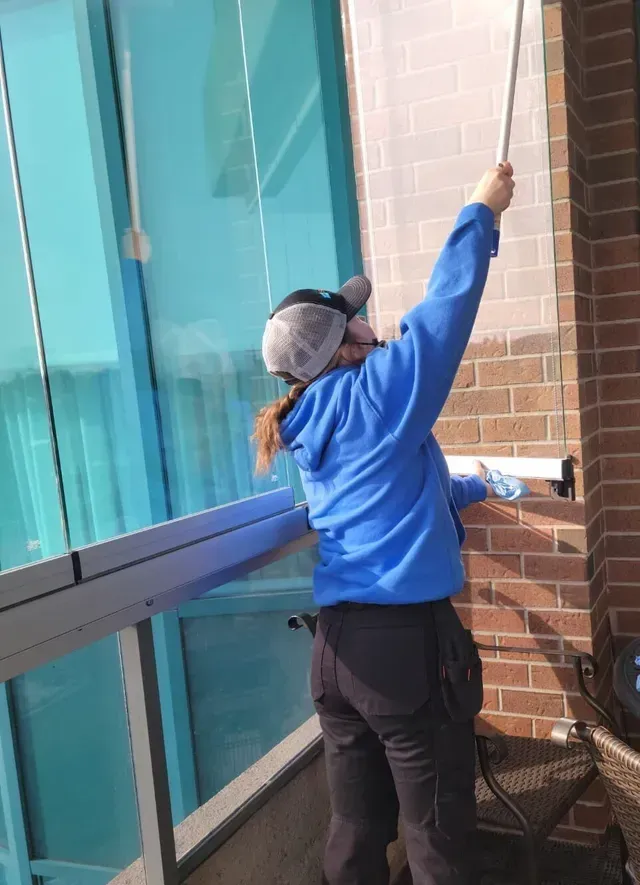 A woman in a blue jacket is cleaning a window