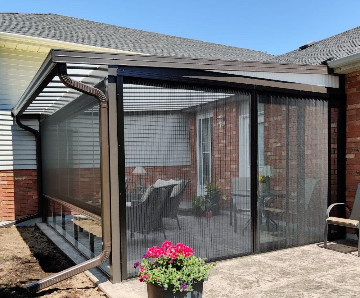 A patio with a screened in porch and a brick house in the background.