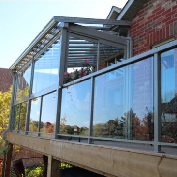 A balcony with a glass railing and a brick building in the background