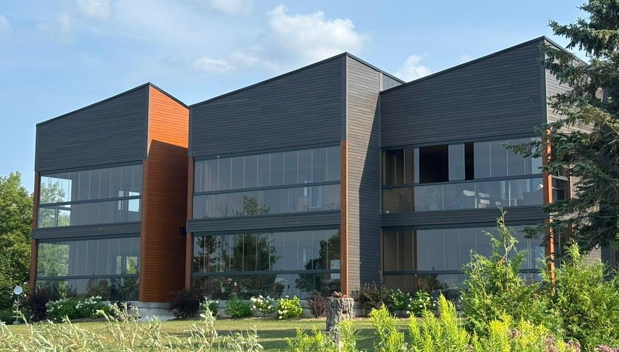 Modern building with dark gray and wood panels, large windows, and a grassy lawn.