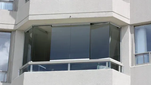 Glass balcony enclosure on a white building, with a partially opened sliding door.