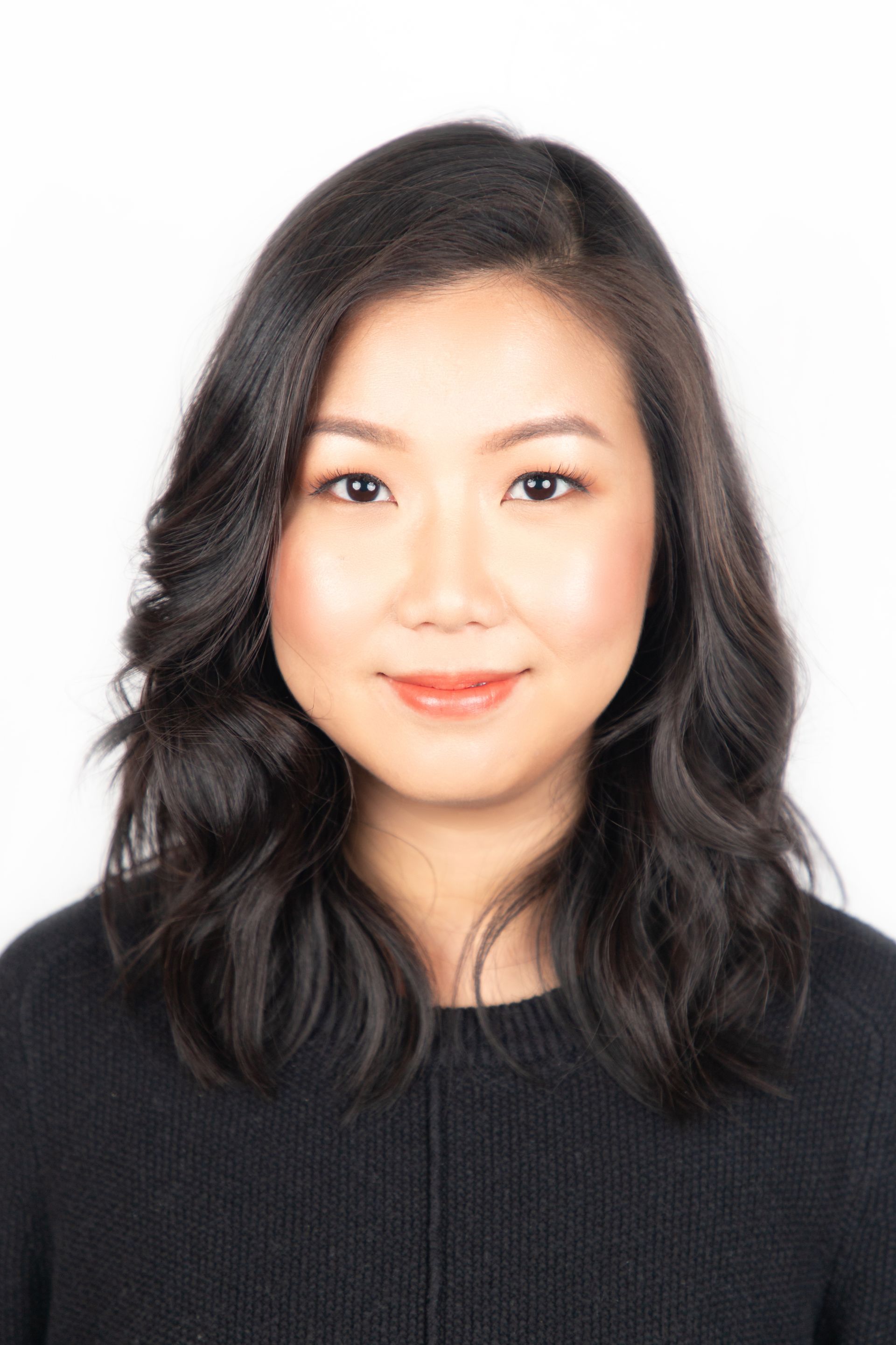 Studio headshot of a woman with wavy dark hair wearing a black top on a white background