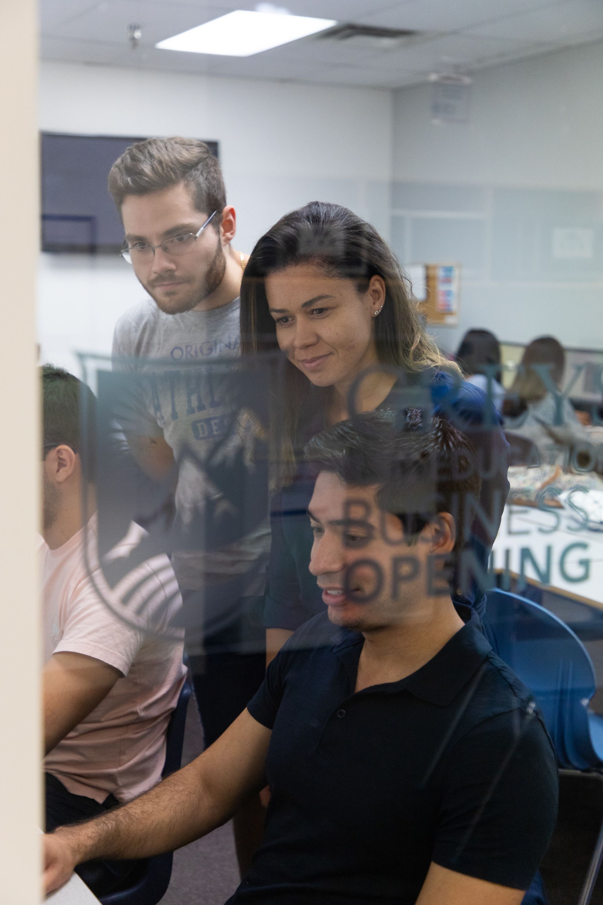 Office meeting through glass wall, with people gathered around a desk and a “Business Opening” sign visible.
