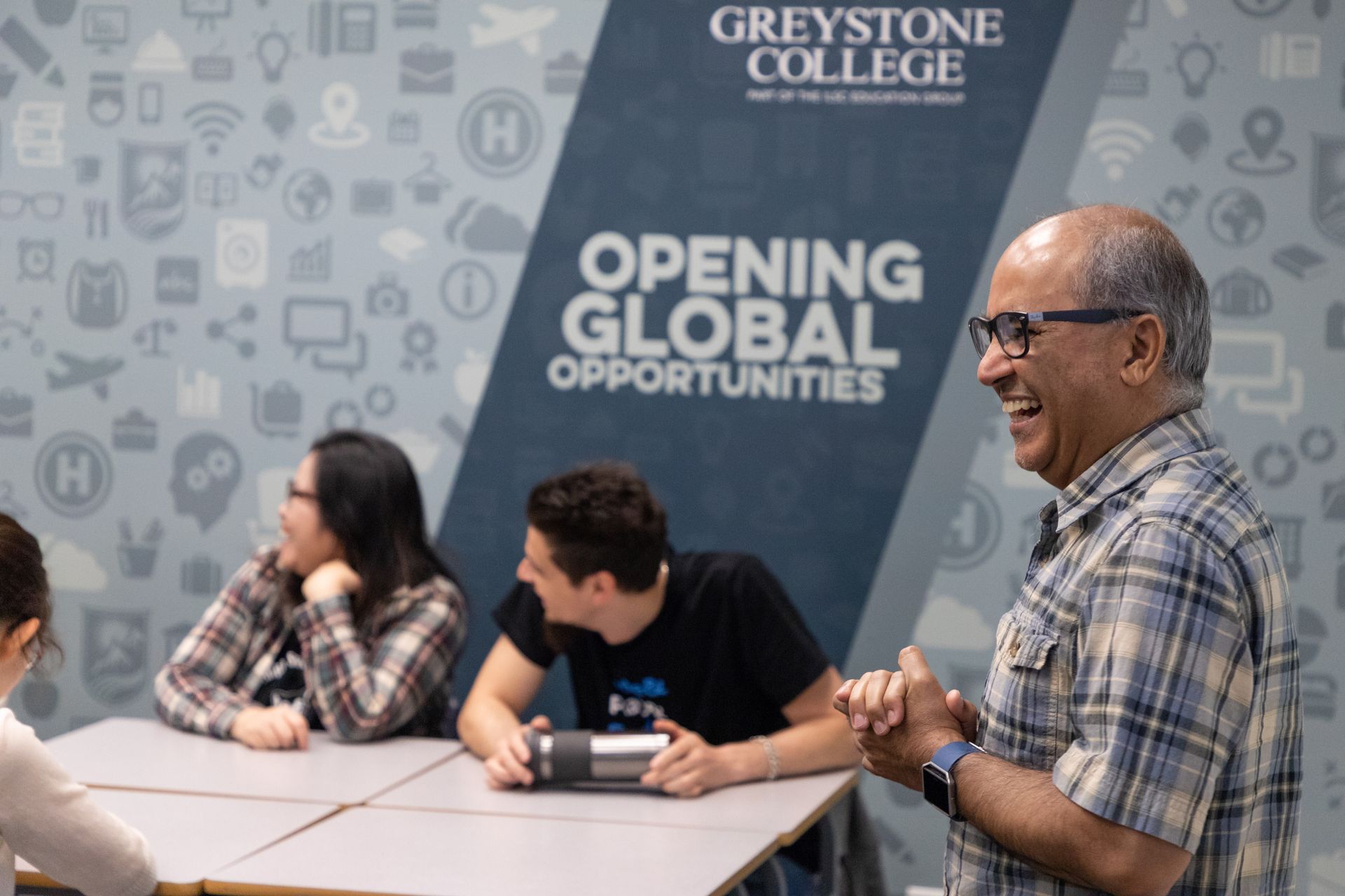 Greystone College event with seated attendees and a smiling speaker beside an “Opening Global Opportunities” sign