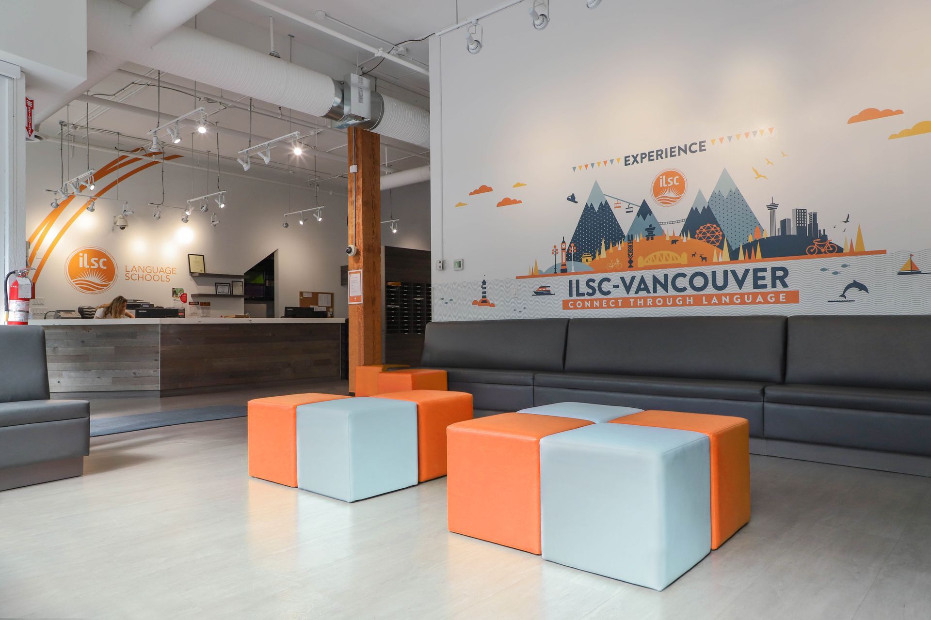 Modern lounge with orange and gray seating and a wall mural reading UBC-Vancouver.