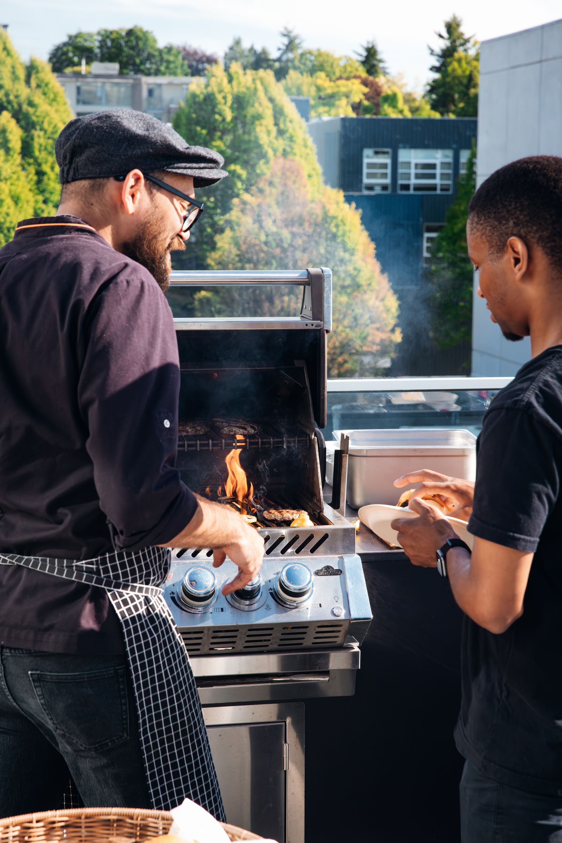 Two people grilling outdoors beside a barbecue in a sunny backyard.