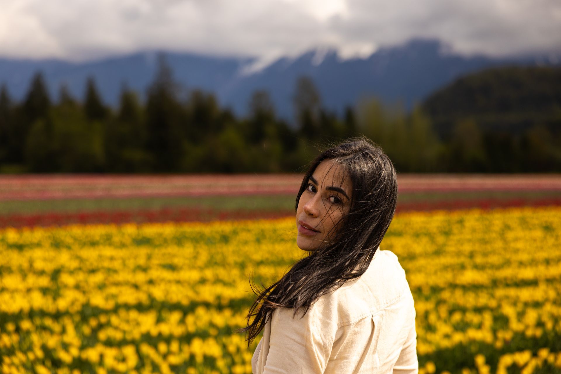 Woman standing in a colorful flower field with mountains in the background