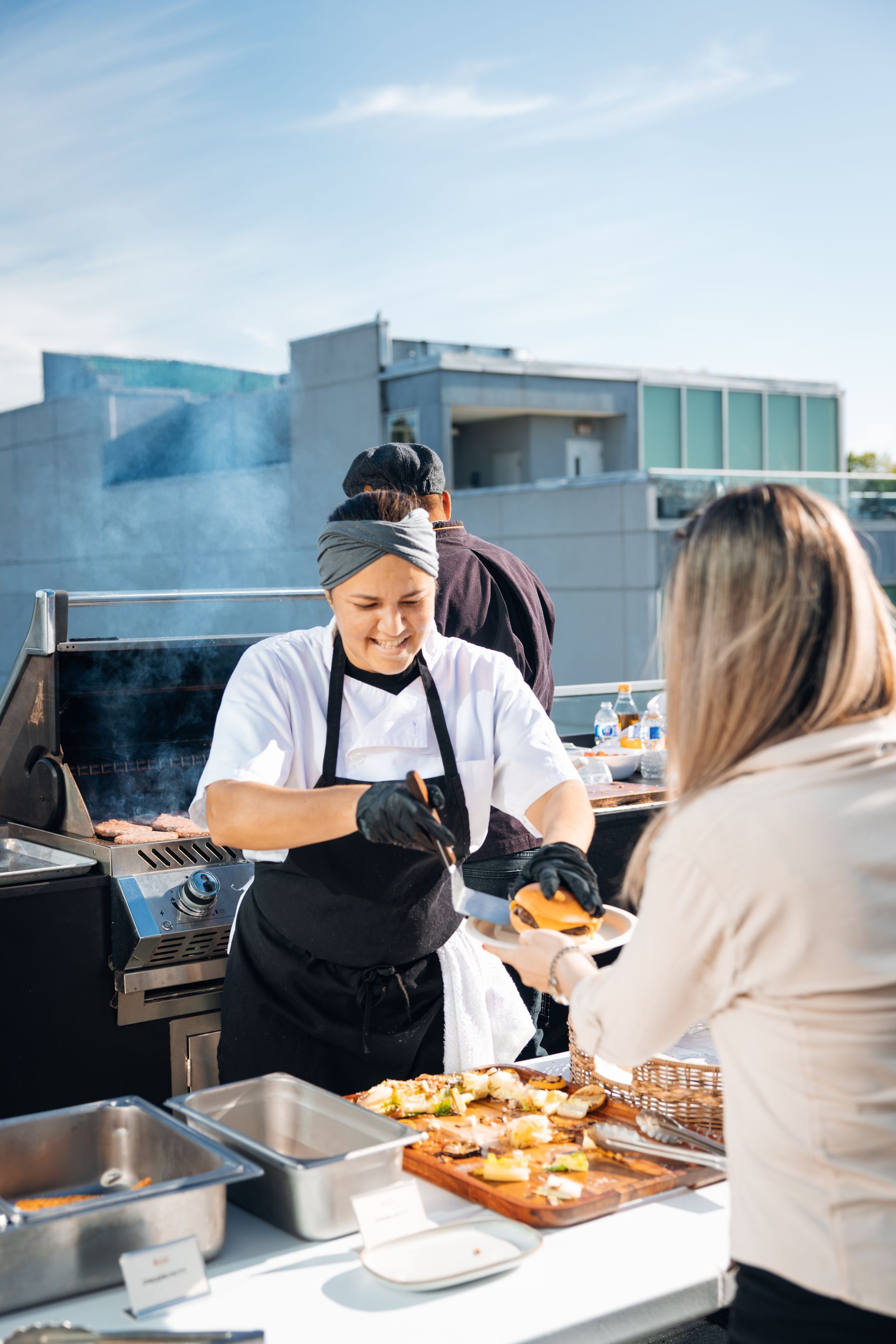 Chef serving food at an outdoor rooftop buffet with city buildings in the background