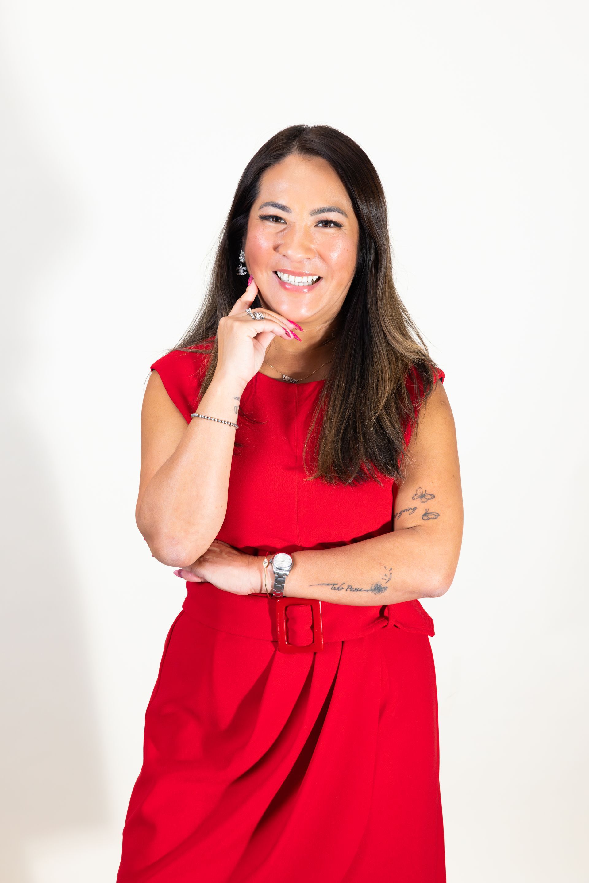 Woman in a red dress smiling with arms crossed against a white background