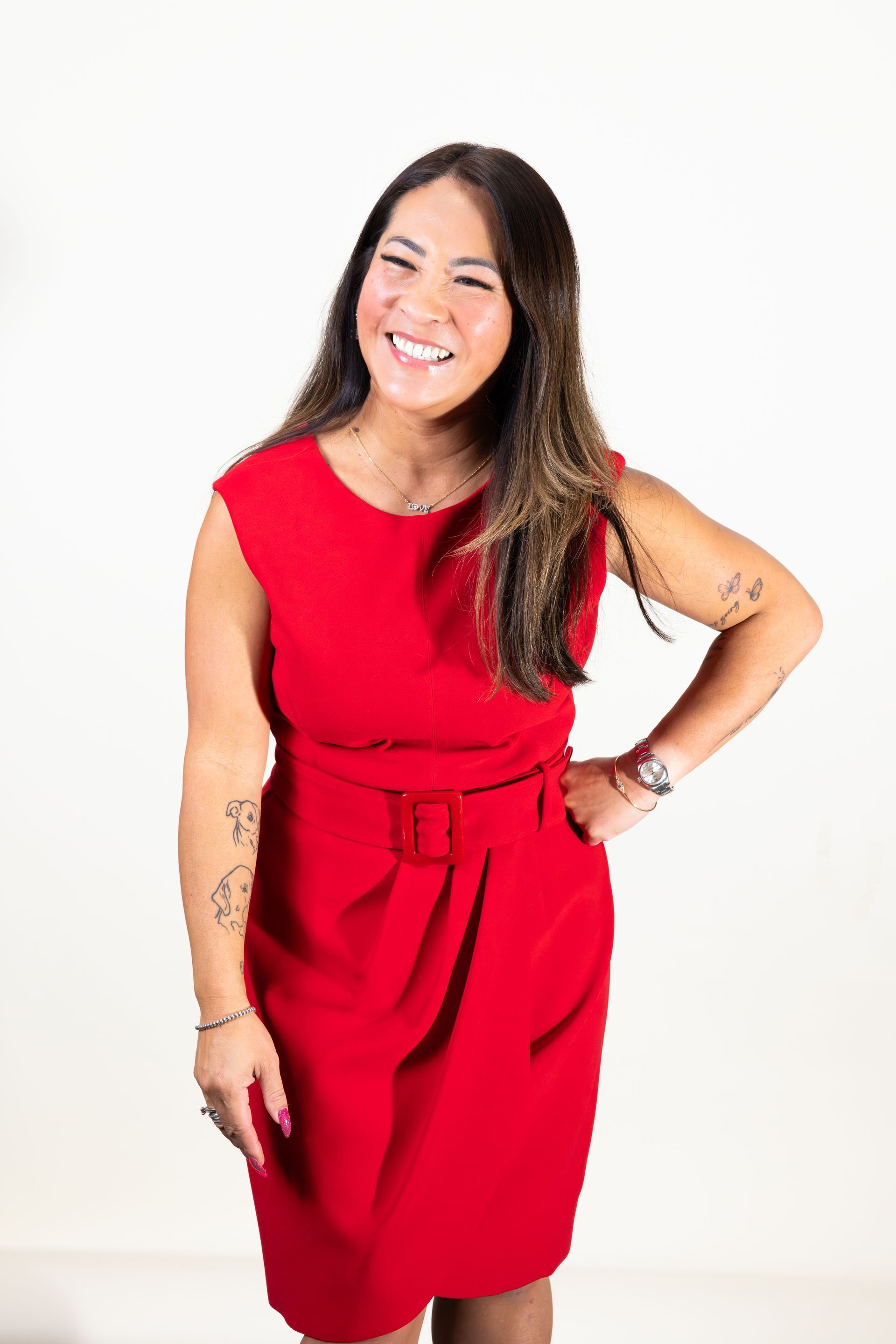 Smiling woman in a red dress standing with one hand on her hip against a white background