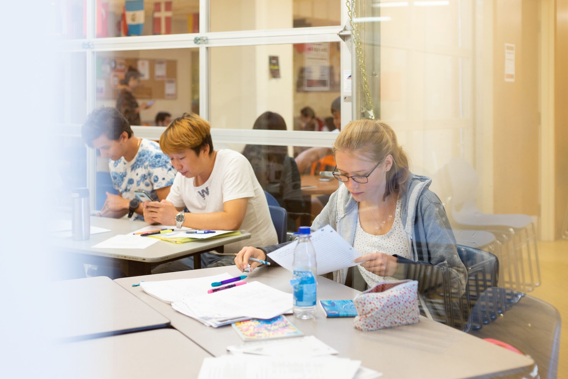 People studying at tables in a bright classroom, writing and reading papers