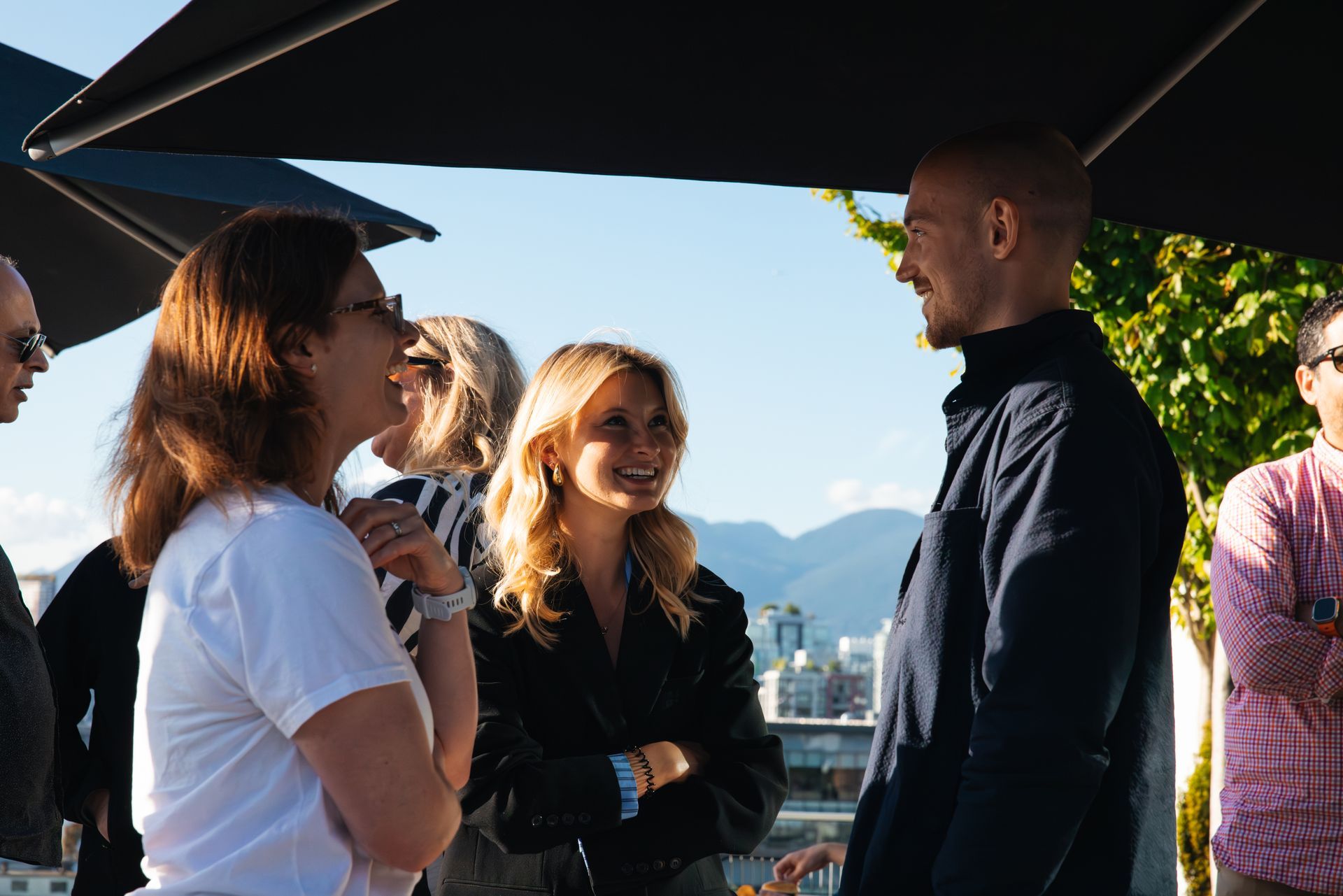 Small group chatting outdoors under dark umbrellas with mountains in the background