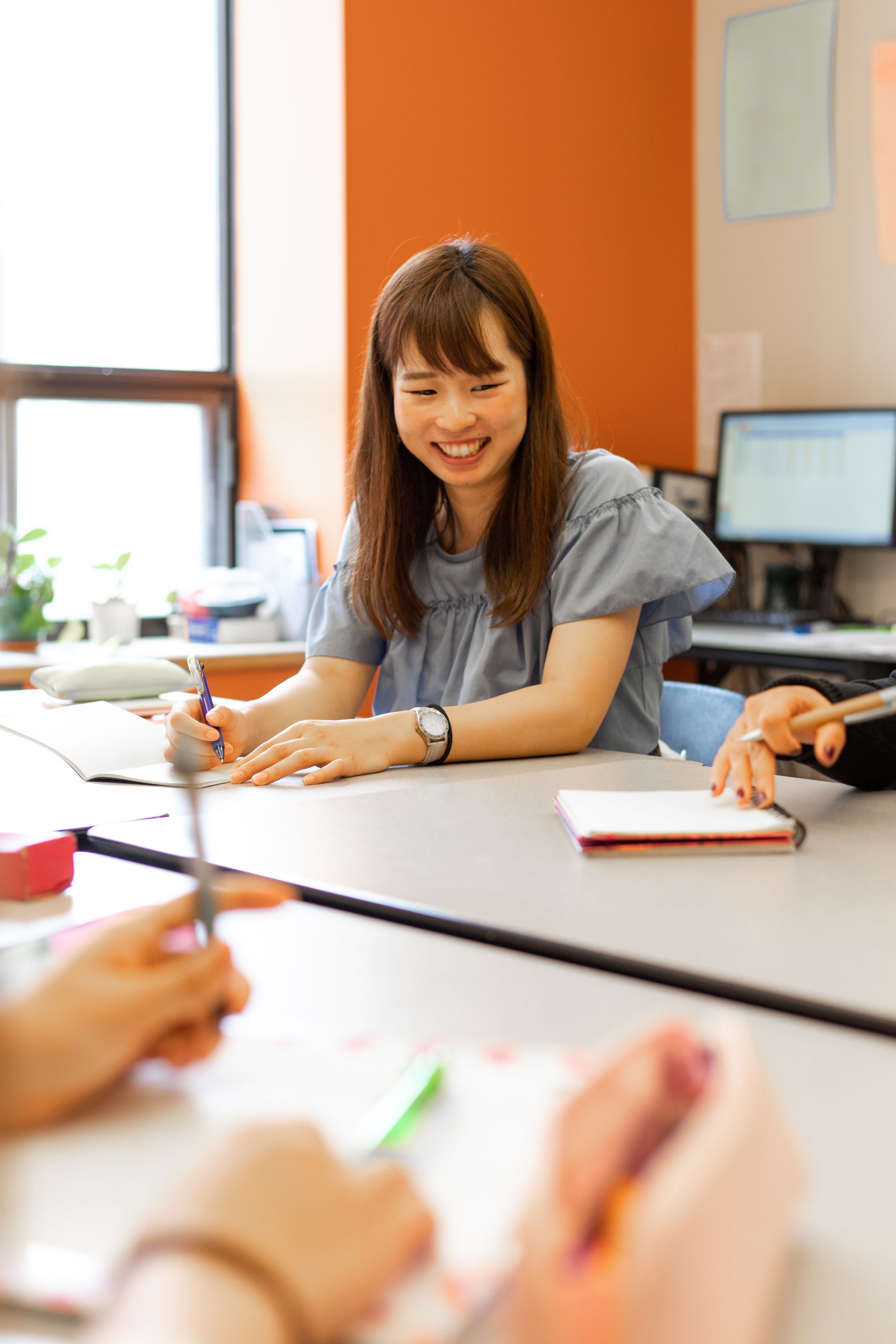 Woman smiling and writing at a meeting table in a bright office classroom