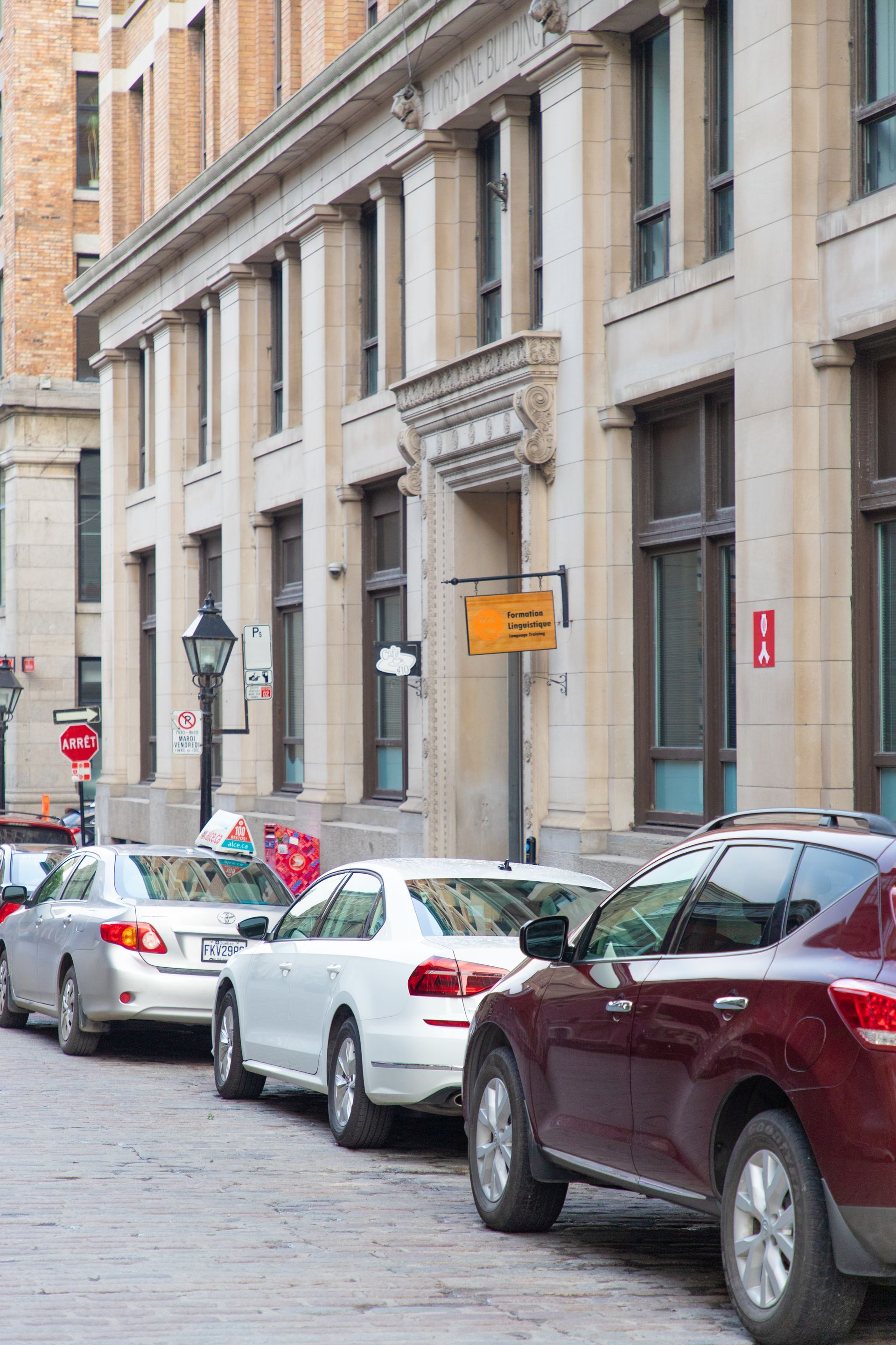 Parked cars lining a narrow city street beside tall stone buildings