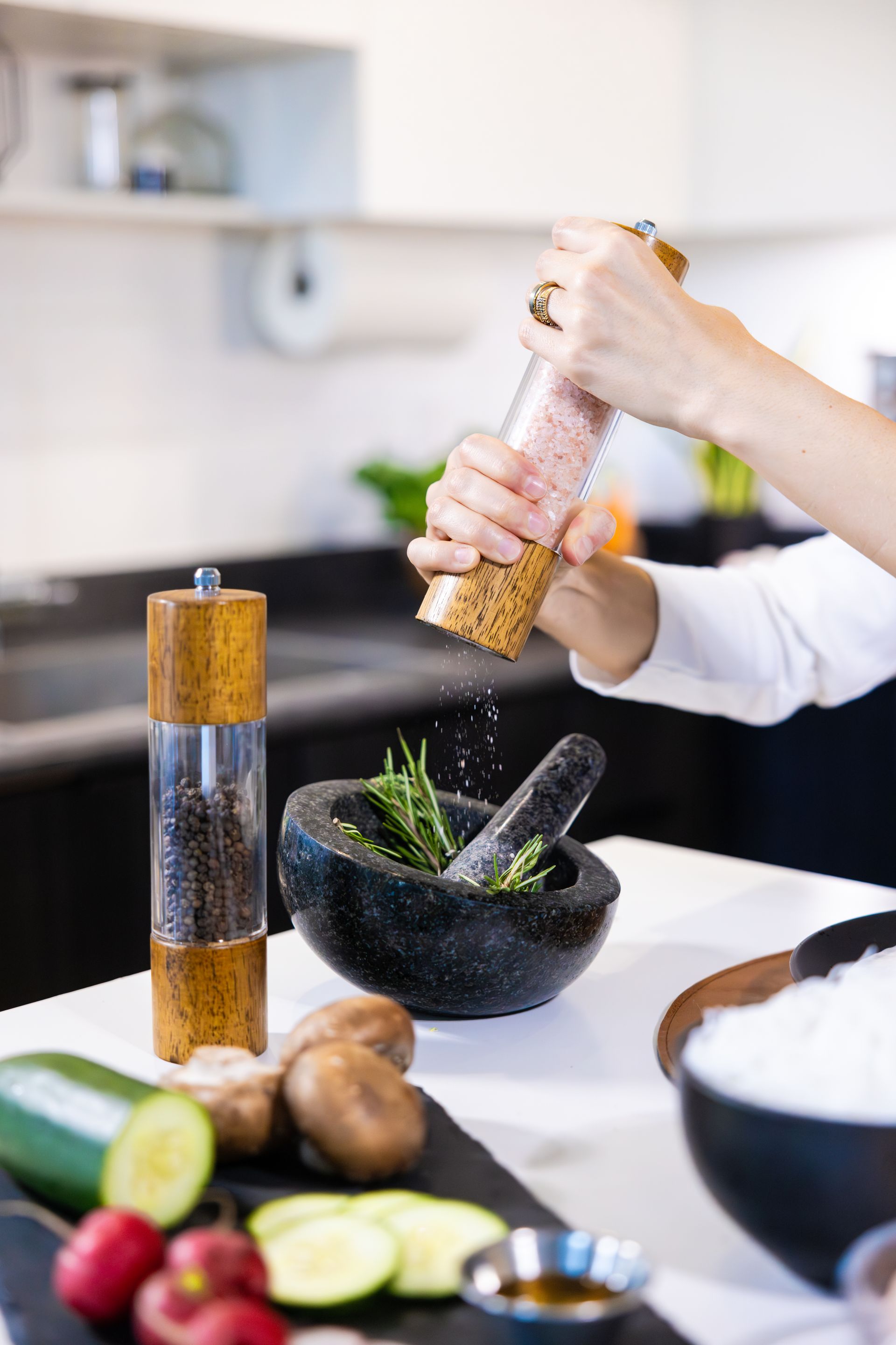 Person seasoning food in a black mortar and pestle in a kitchen with sliced vegetables nearby