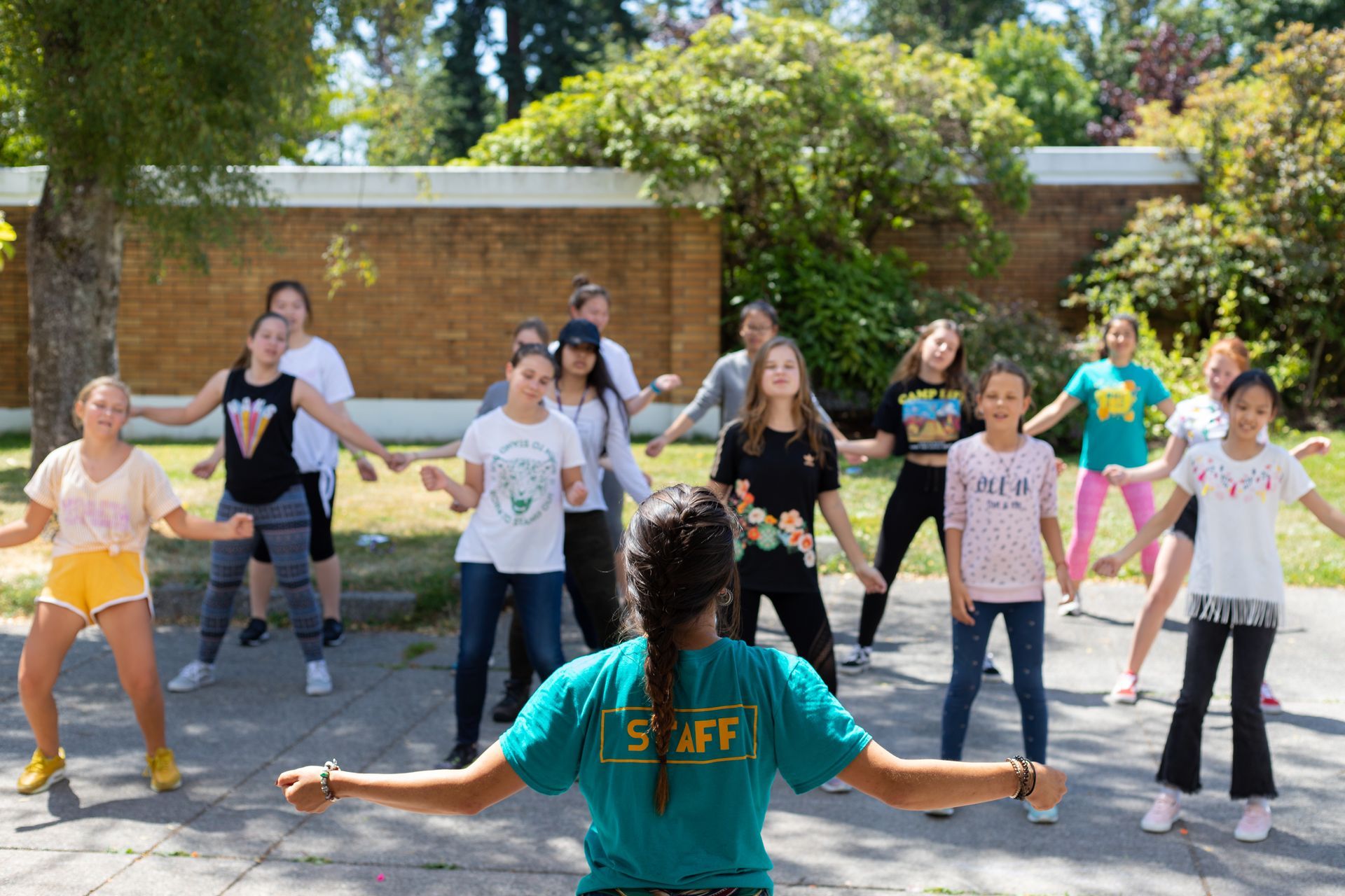 Instructor leading a group dance class outdoors in a sunny courtyard, participants following along