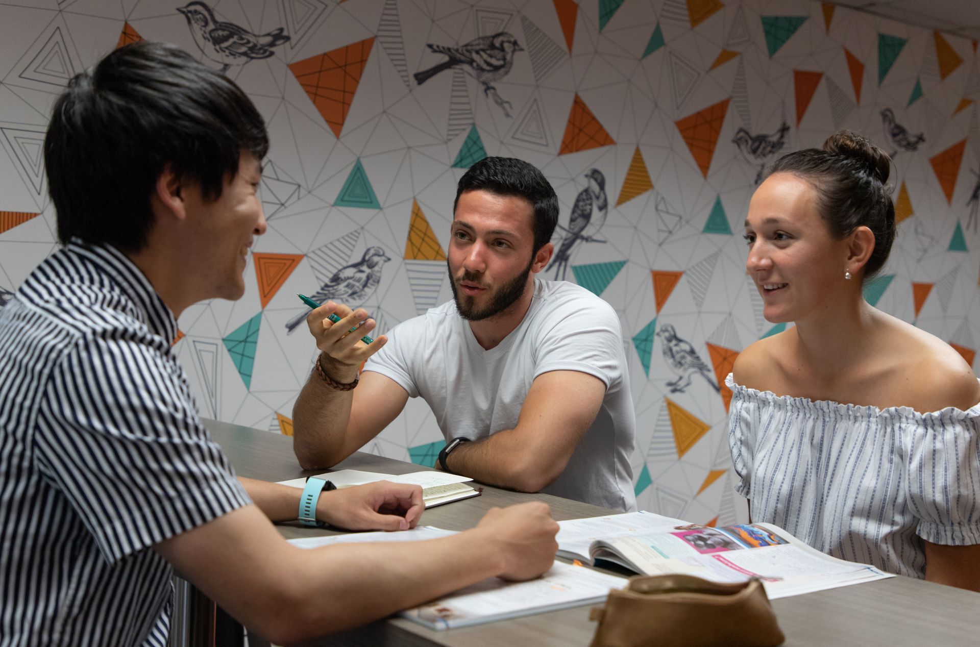 Three people in a meeting, discussing ideas around a table with papers and a notebook