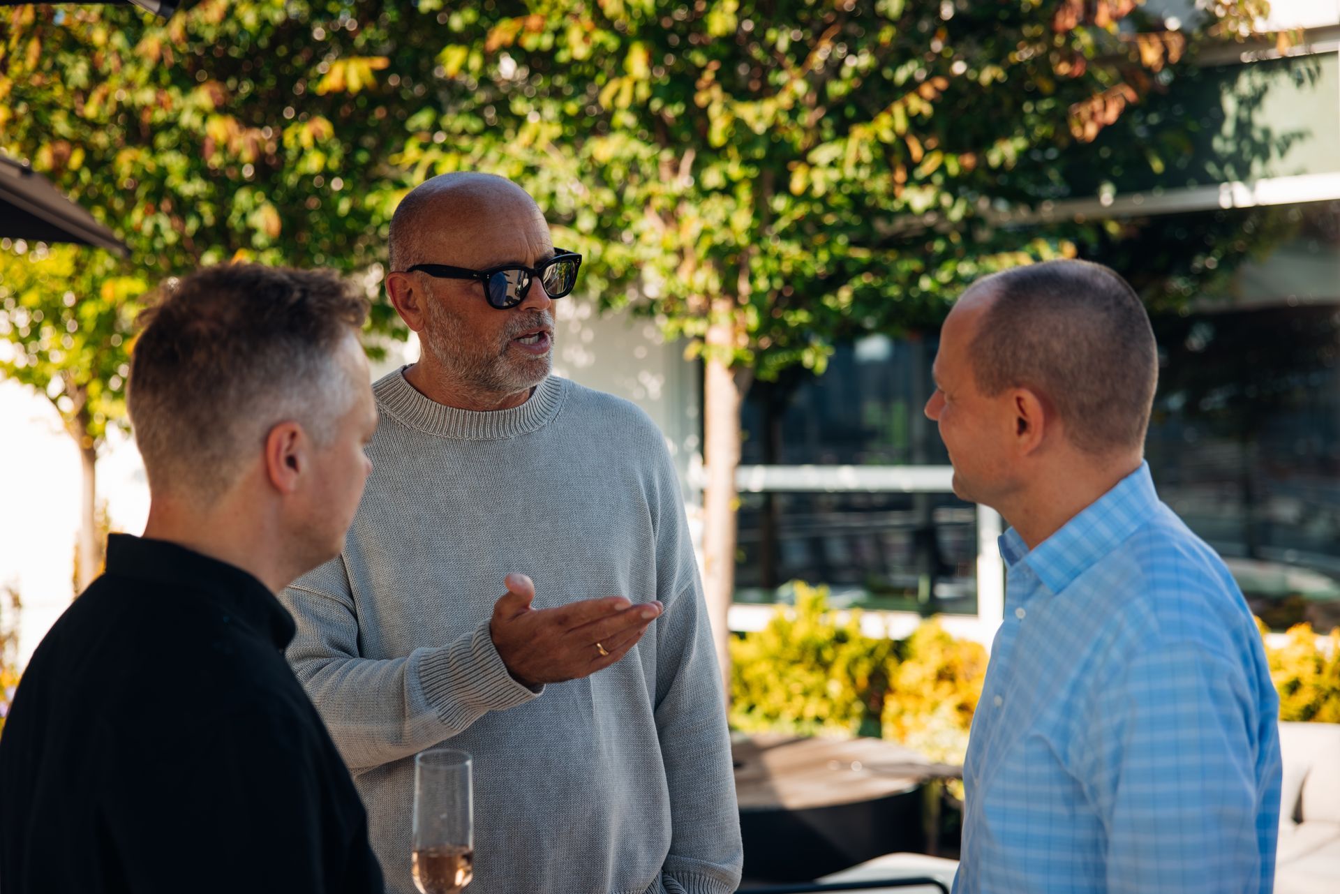 Three people talking outdoors, with one gesturing during a conversation.
